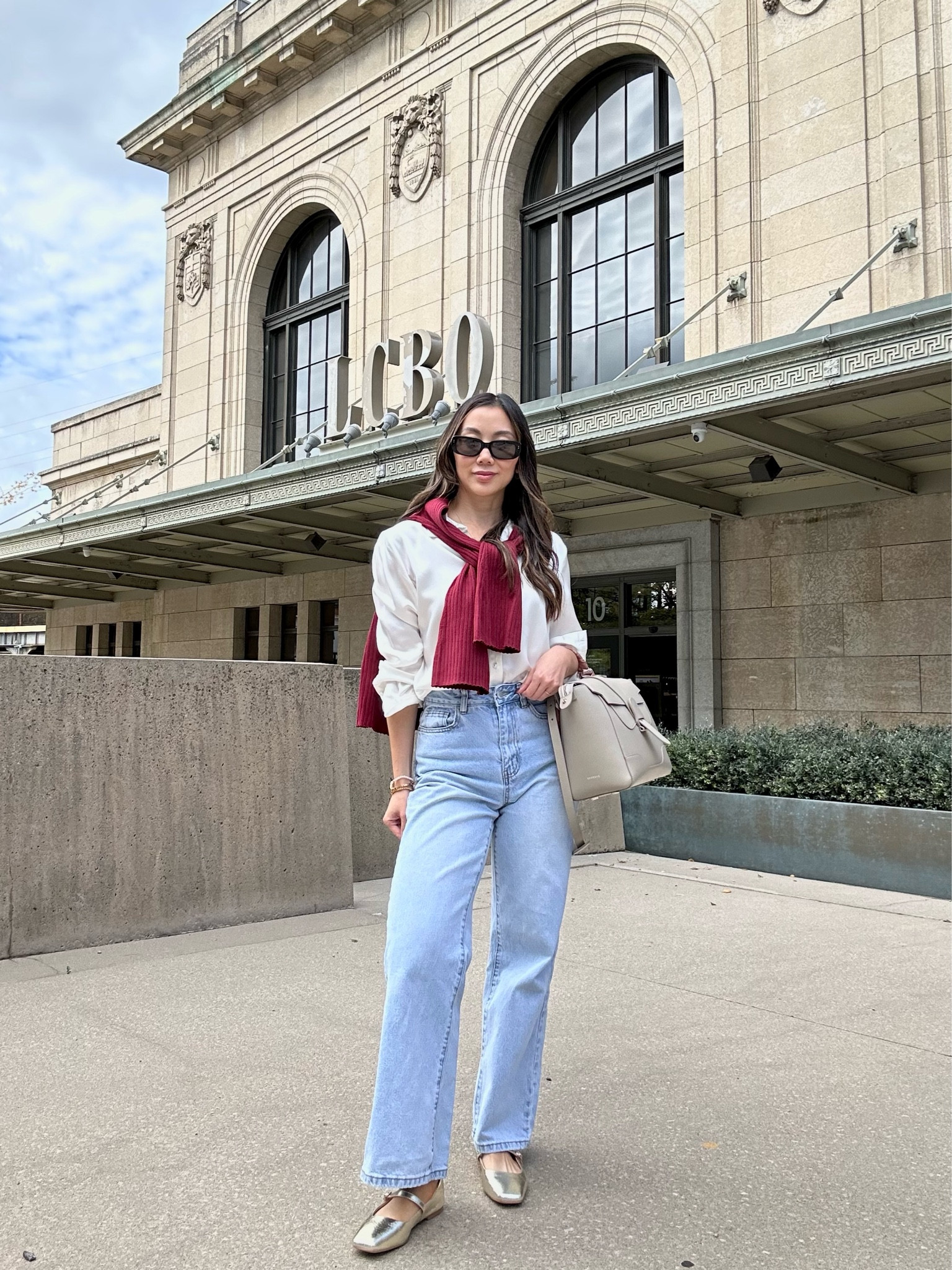 Classy fall outfit idea with burgundy cardigan paired with a button-down shirt, shirt and wide leg jeans. Ass accessorized with a classic bag and gold ballet flats along with some rectangular sunglasses to complete this fall French girl outfit. 