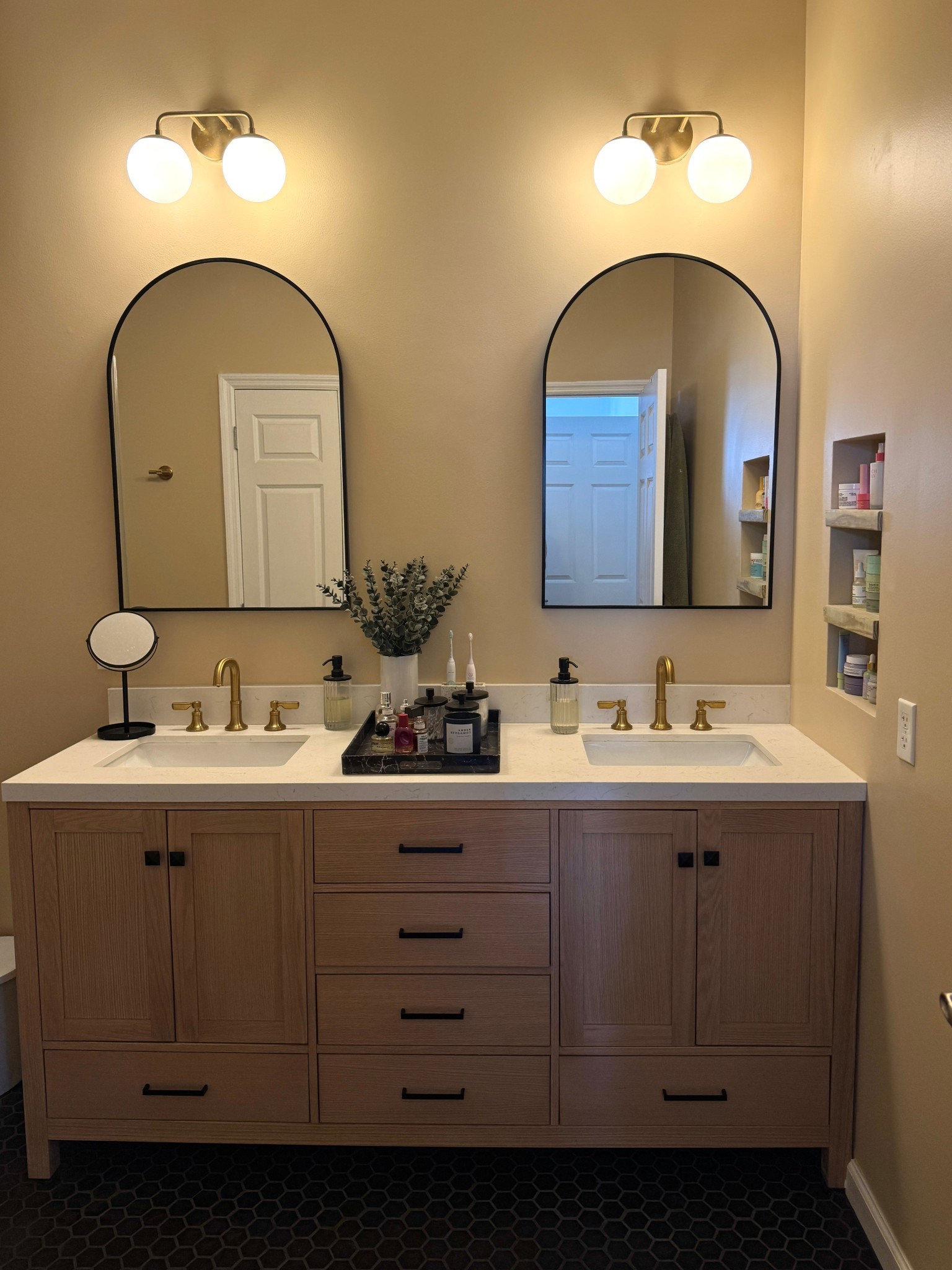 The results of our renovated primary bathroom! I love how it turned out. The double vanity is from The Home Depot and so are the faucets we selected. We added two double arch mirrors outlined in black to match the hardware on the vanity and then two double vanity lights above. Then on top of the vanity there’s a round mirror, two soap dispensers and a black marble tray. I also chose to do a black hexagon tile for the floor! 

#LTKHome #LTKFindsUnder100