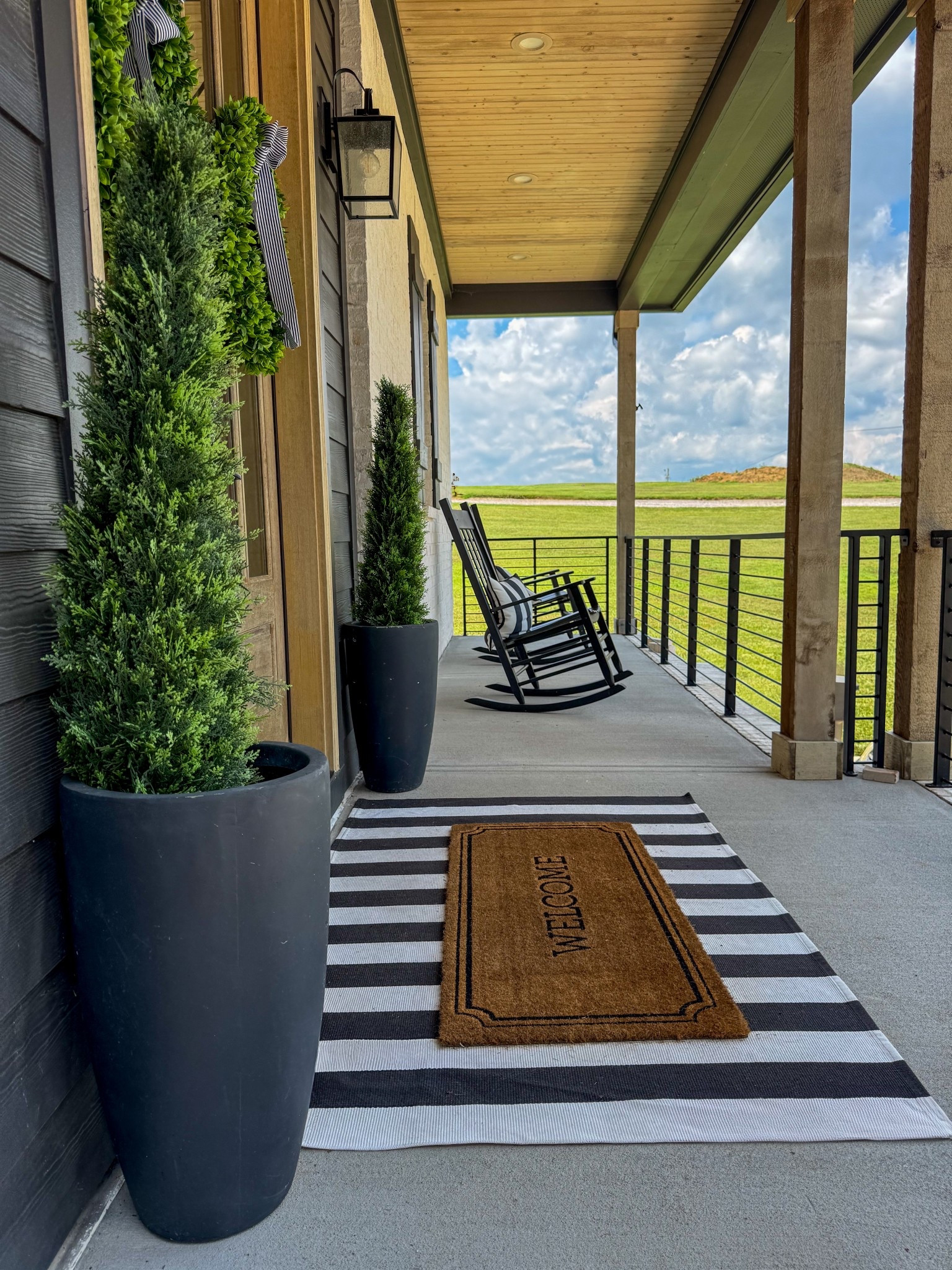 Front porch decor 🏡 
extra large striped outdoor welcome mat, 

faux topiary cedar tree outdoor plants, black planter, black rocking chair, striped outdoor rug, welcome doormat, boxwood wreath, modern farmhouse front porch decor, outdoor entryway decor #frontporch 

#LTKHome #LTKSeasonal