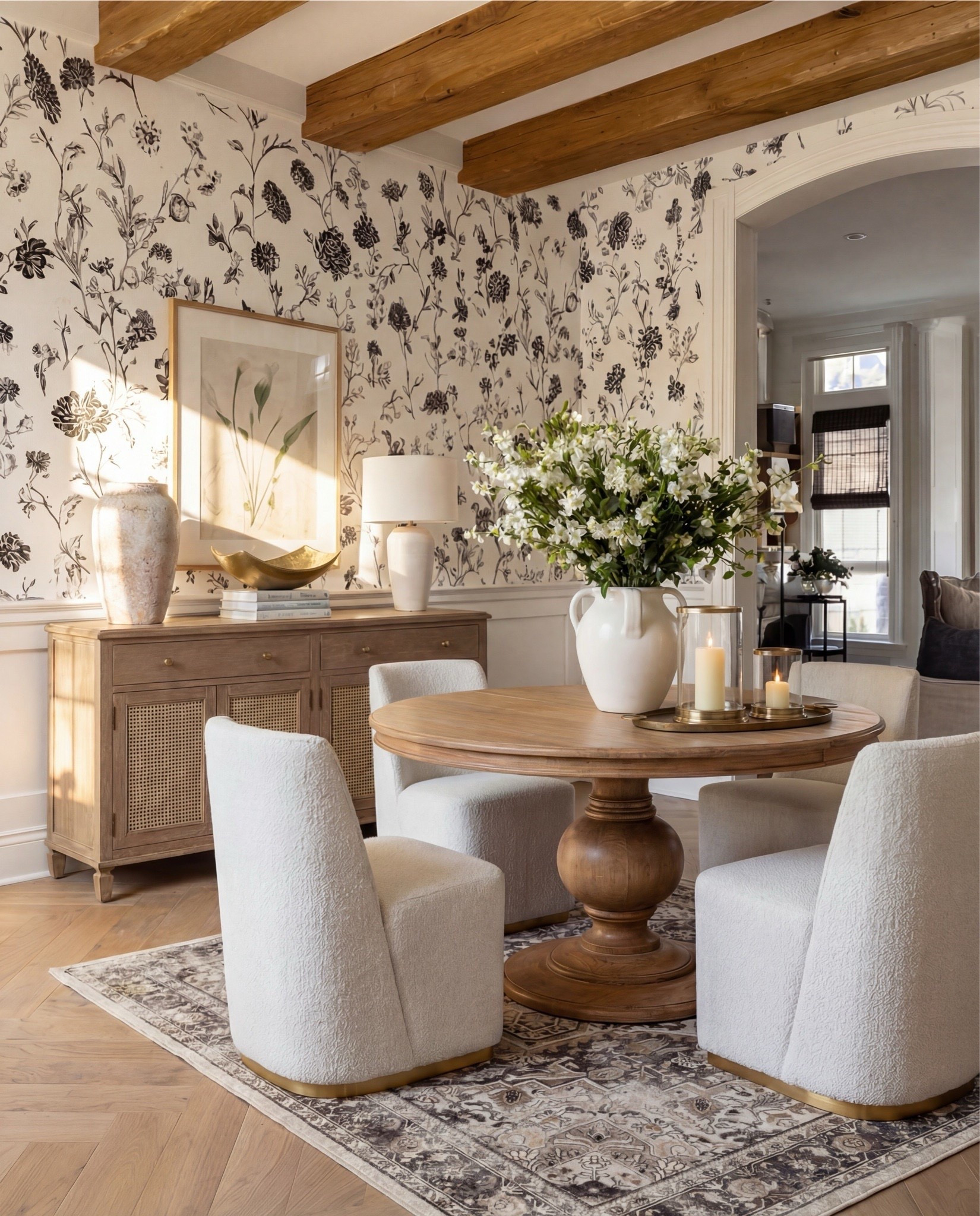 Warm, intimate, and beautifully layered — this dining nook blends soft neutrals with rich wood textures for a cozy, elevated moment. The round pedestal table brings sculptural warmth, while the cream upholstered chairs add a soft, modern edge. The black-and-cream floral wallpaper creates a refined backdrop, and the cane-front sideboard adds the perfect touch of artisanal texture. Finished with brass accents, fresh florals, and candlelight, this space feels effortlessly refined.

Shop the Look:
• Round natural wood pedestal dining table
• Cream textured upholstered dining chairs
• Black & cream floral wallpaper
• Light oak cane-front sideboard
• White sculptural ceramic vases
• Brass decorative bowl
• Neutral framed botanical artwork
• Brass candle tray with glass hurricanes
• Vintage-style distressed area rug
• White floral arrangement in large ceramic pitcher


#LTKHome #LTKSaleAlert