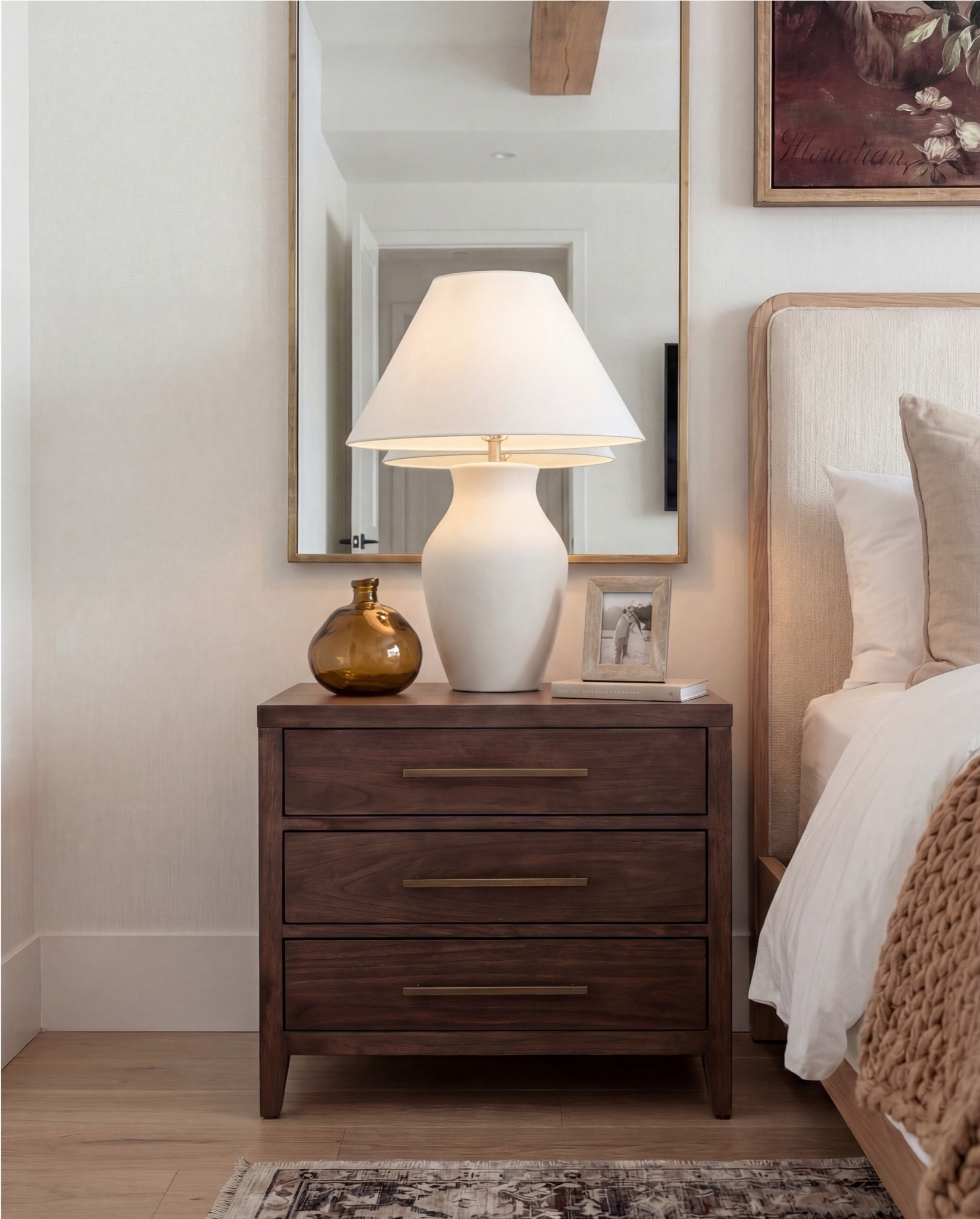 This bedroom feels warm, grounded, and quietly luxurious. Soft neutral layers and rich wood tones create an inviting, hotel-like calm, while the exposed wood ceiling beams add architectural character and warmth. The upholstered bed keeps the space feeling serene and tailored, balanced by cozy textures and subtle brass details that bring depth without overpowering the room.

The styling is refined and intentional—clean lines, natural materials, and a mix of classic and sculptural accents that make the space feel timeless, restful, and thoughtfully lived-in.

Shop the Look: Bedroom Refresh
• Upholstered bed frame (light neutral fabric)
• White cotton duvet cover + pillow shams
• Neutral patterned area rug
• Chunky knit throw blanket (warm beige)
• Woven knit poufs (foot-of-bed seating)
• Dark wood nightstands with brass pulls
• Sculptural white ceramic table lamps
• White tapered lamp shades
• Brass-framed rectangular mirrors
• Framed floral artwork (warm, moody tones)
• Neutral linen accent pillows
• Ceramic decorative bowl (white sculptural style)
• Small glass vase with white florals

#LTKSaleAlert #LTKHome