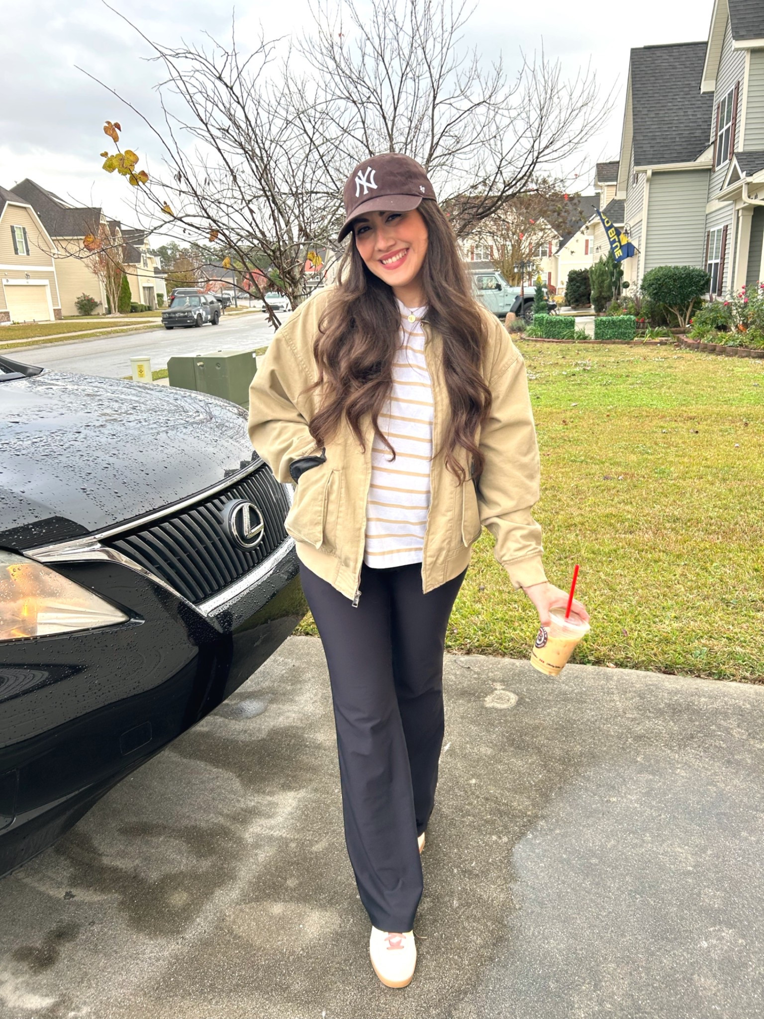 Tan bomber jacket
Barn jacket 
Black flared leggings 
Brown NY baseball cap hat 
Striped t shirt