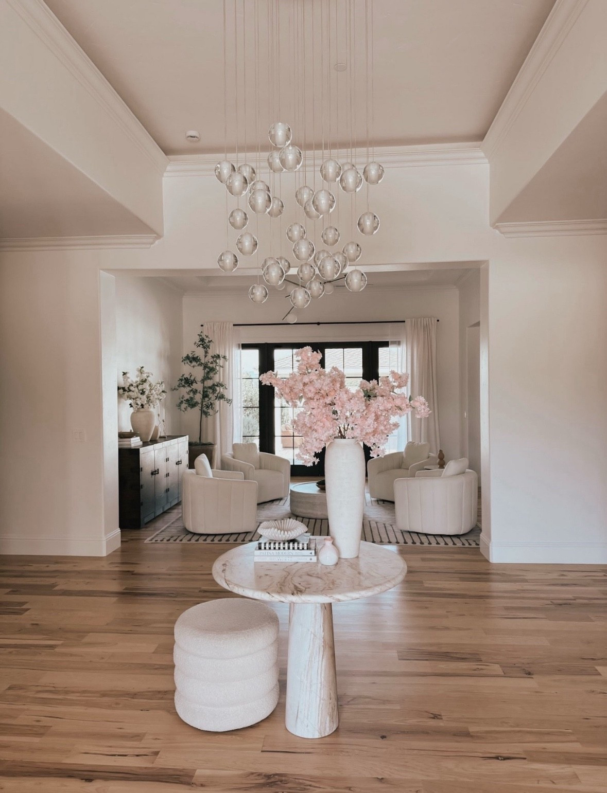 Entry way drop chandelier with a round marble table and boucle stool 

