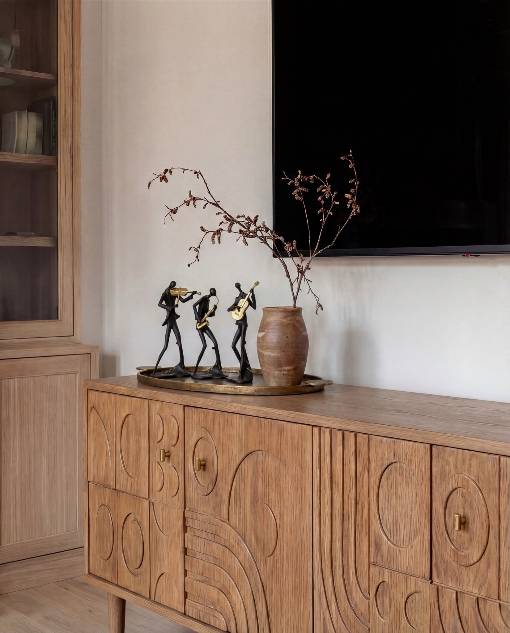 Shop the Look:
• White upholstered sofa (clean-lined, low profile)
• White upholstered armchairs (pair)
• Light wood round coffee table (fluted or ribbed base)
• Neutral vintage-style area rug (muted brown and beige tones)
• Marble fireplace surround
• Black fireplace insert
• Large framed landscape wall art (soft blue and neutral tones)
• Brass wall sconces (pair, globe style)
• White globe pendant light with brass detail
• Natural wood ceiling beams
• Light wood flooring

Coffee Table Styling:
• Large white ceramic vase (rustic sculptural style)
• Decorative hardcover books (neutral covers)
• Gold abstract heart sculpture
• Brass oval tray
• Decorative brass object (sculptural accent)

Sofa Styling:
• Neutral throw pillows (warm beige)
• Chunky knit throw blanket (camel or warm brown)

Media Console Area:
• Light wood sideboard / media console (carved front detail)
• Brass cabinet knobs
• Black figurine sculptures (musician figures, set of three)
• Brown ceramic vase
• Dried branches / minimalist floral stems
• Brass decorative tray

#LTKHome #LTKSaleAlert