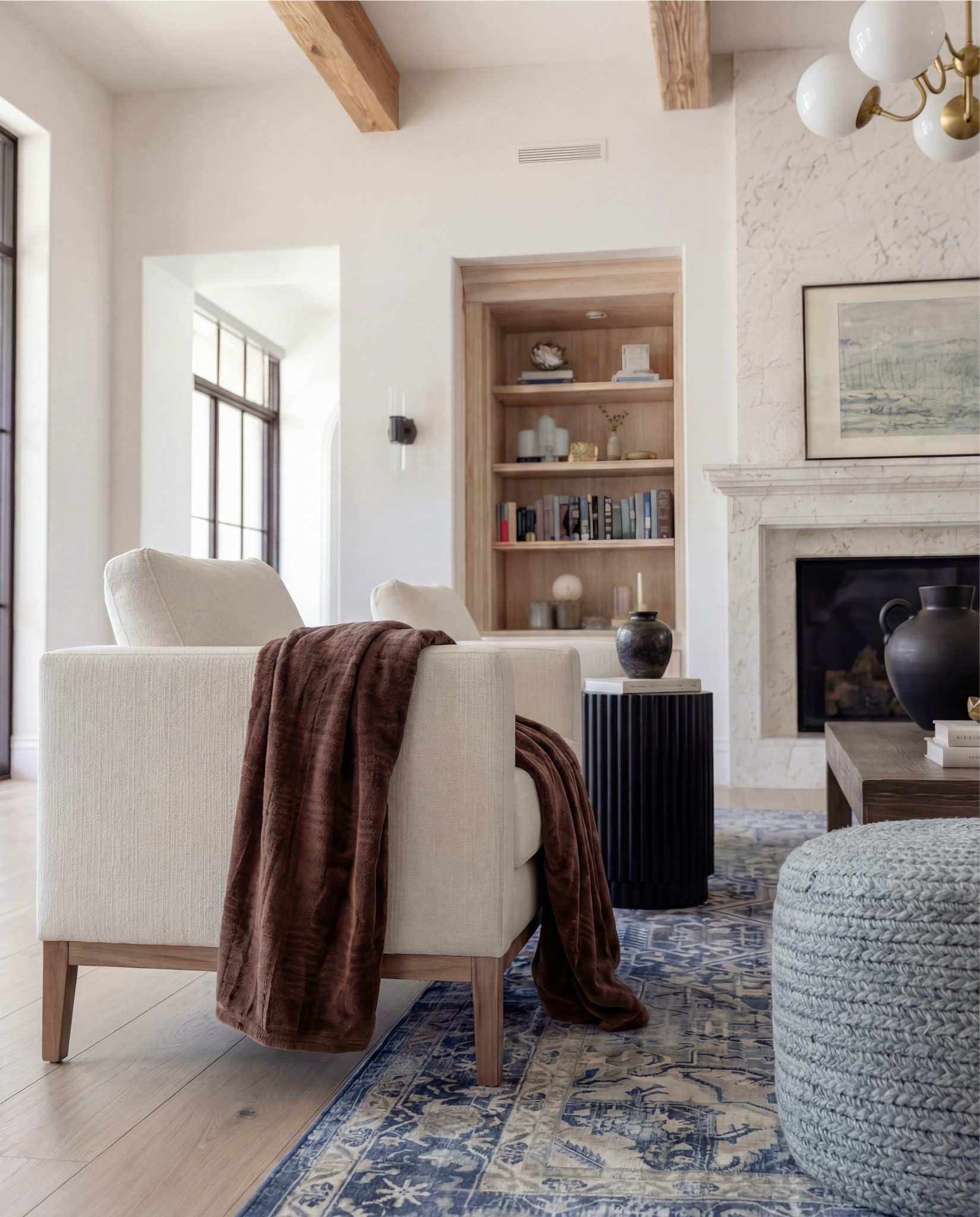 Shop the Look:
• Marble fireplace surround
• Cream armchairs + sofa
• Blue patterned lumbar + throw pillows
• Chunky knit ottomans
• Solid wood coffee table
• Black ceramic vase decor
• Distressed blue traditional rug
• Wood built-ins with glass fronts
• Warm wood ceiling beams
Brown throw blanket 
White decor books
Brass oval tray
Black decor bowl
Rounded globe chandelier 

#LTKHome #LTKSaleAlert