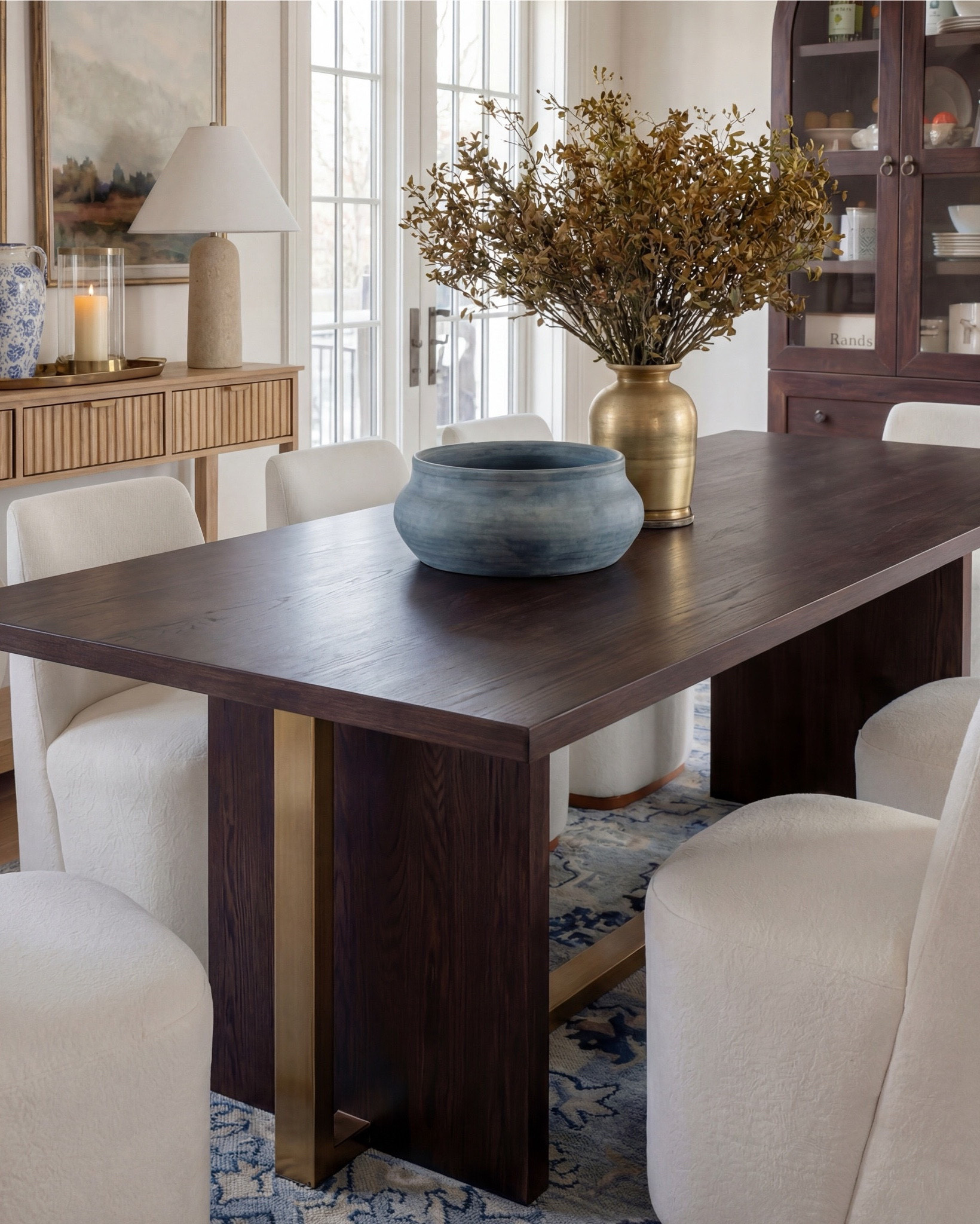 This dining room feels calm, intentional, and quietly elevated. The exposed wood beams warm up the space, while soft blues—on the ceiling and rug—bring in that serene, lived-in charm. The contrast between the dark wood table and the plush ivory chairs makes everything feel grounded yet refined.

The styling really sells it: a blue ceramic bowl centered on the table, a brass vase with organic branches for height, and layered decor along the sideboard that keeps the room from feeling too formal. It’s traditional at its core, but styled in a way that feels fresh and current.

Shop the Look:
• Dark wood rectangular dining table
• Curved ivory upholstered dining chairs (wood base)
• Blue ceramic decorative bowl (table centerpiece)
• Brass vase with dried branches
• Blue patterned area rug
• Light wood sideboard with fluted drawer detail
• Blue-and-white ceramic vase (sideboard)
• Neutral table lamp with white shade
• Stacked books + candle decor
• Framed landscape wall art (set of two)
• Dark wood arched china cabinet with glass doors
• White ceramic floor vase
• Exposed wood ceiling beams
• Soft blue ceiling paint
• Tall floor vase

#LTKsale #LTKhome #LTKstyletip