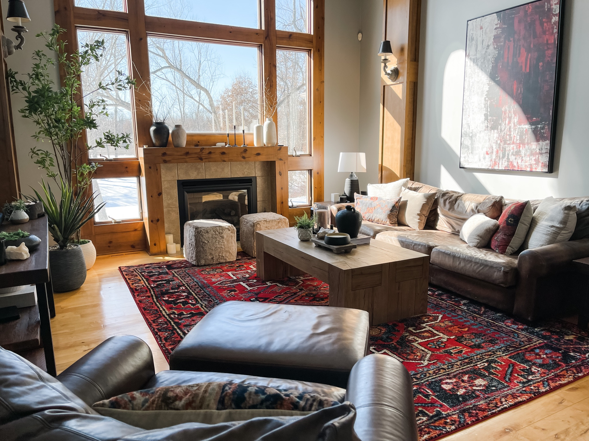 In this living room we have a red oriental rug, red abstract wall art, coffee table, table decor, tray, small plant, vase, pillar candle, candle holder and stand, poof stools, leather couch, leather chair, leather ottoman, fireplace, table lamp, side table, console table, large plants, pots, branches, candlesticks, candlestick holders, and wall sconces.

#LTKhome