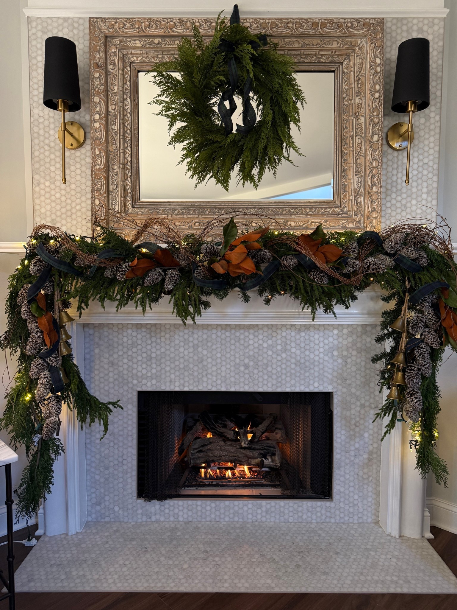 Christmas mantel 2025. I’m going with a large wood carved mirror with a wreath over the top. Lush garland mixed with twinkle lights, magnolia, grapevine garland, pine cones and a mix of greenery!

#LTKHome #LTKSeasonal #LTKHoliday
