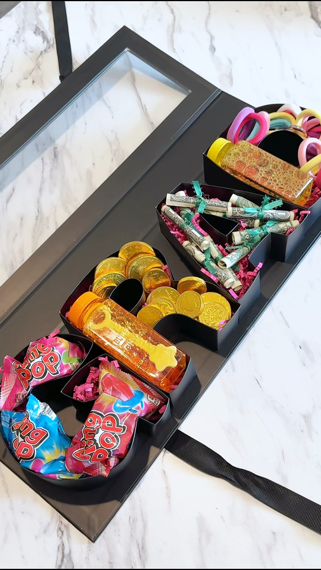 The cutest graduation gift for the little kidergarten grad! 🎓📚🩷✏️

Y'all l'm telling you these word gift boxes make the cutest little gifts I'm obsessed! They are so easy to fill with all the favorite things making them personalized and something they will love!

Included in GRAD box:
🖤Bubbles
🖤Gold coin chocolates
🖤Hair ties
🖤Ring pops
🖤Diploma dollar bills

#LTKGiftGuide #LTKParties #LTKKids