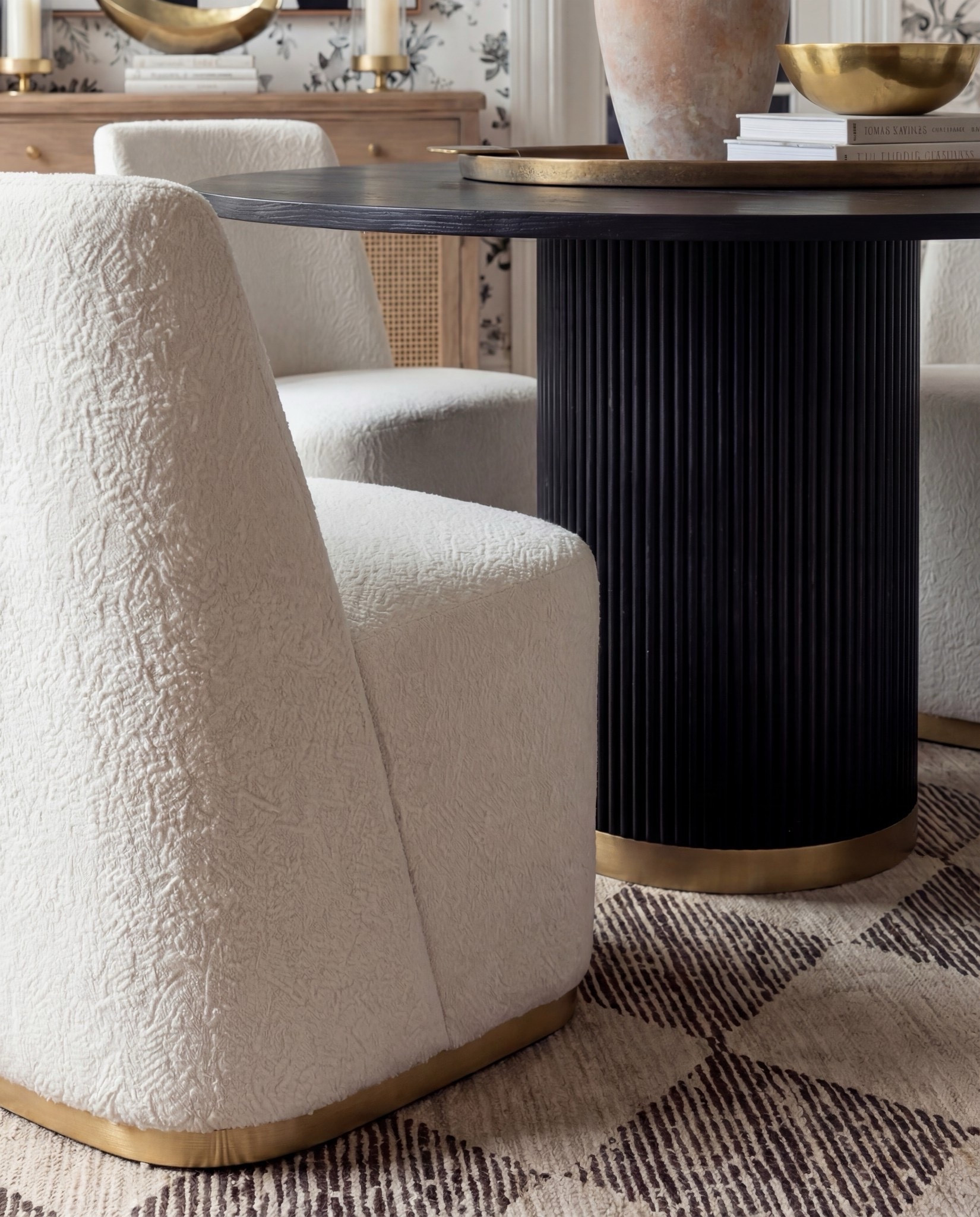 Shop the Look:
• Black fluted pedestal dining table with brass base
• Cream textured barrel dining chairs with brass foot detail
• Black & ivory floral wallpaper
• Soft geometric neutral area rug
• Light oak sideboard with rattan door insets
• Oversized abstract black-and-white wall art
• Terracotta ceramic vase with florals
• Black sculptural ceramic jar
• Brass decorative bowl
• Neutral hardcover styling books
• White glass globe pendant light



#LTKSaleAlert #LTKHome