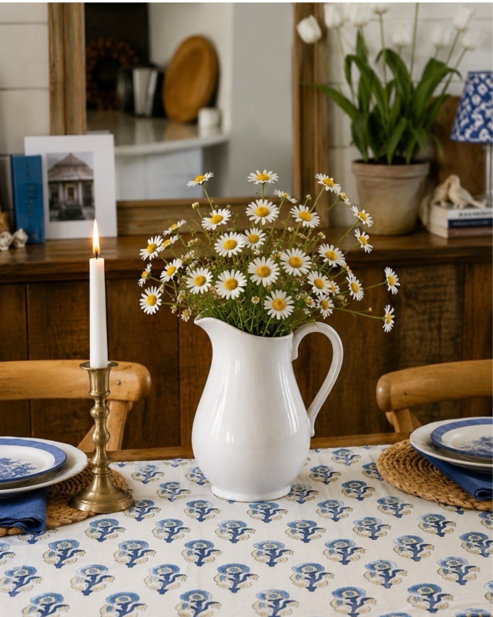 A simple white pitcher filled with cheerful faux daisies is one of my favorite ways to bring timeless cottage charm to a table. Paired with a beautiful blue-and-white runner and classic details, this look feels fresh, welcoming, and easy to recreate. I’ve linked everything you need to create this effortless floral centerpiece and cozy, collected style in your own home. 
#florals #faux #pitcher #runner #candlestick #entertaining