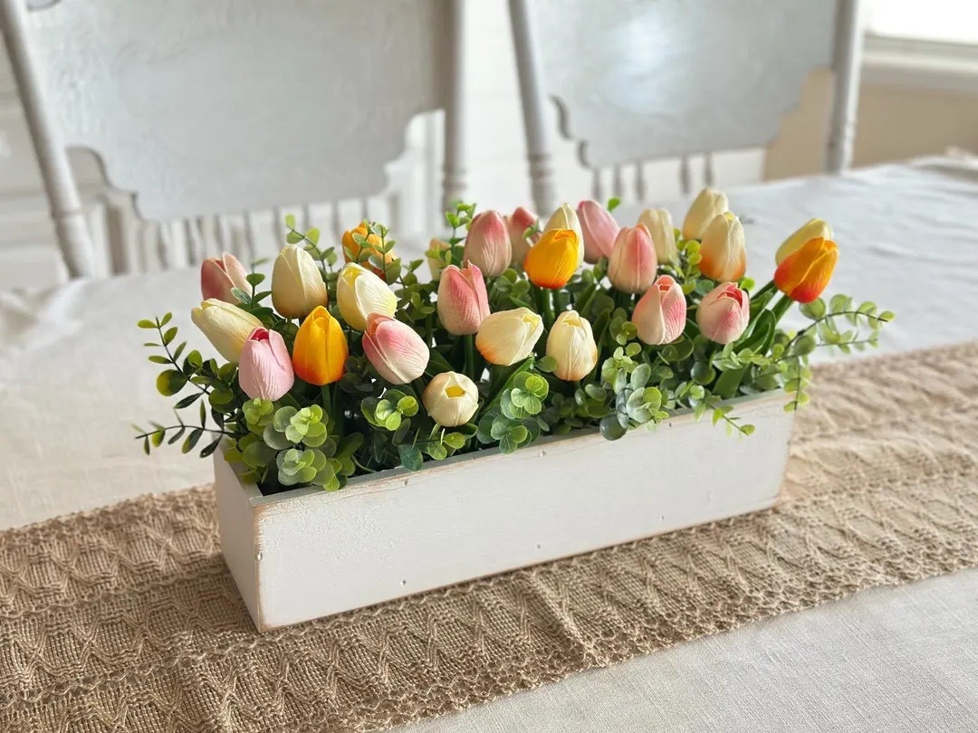 Brighten your home with this cheerful tulip arrangement, designed to capture the fresh beauty of spring all year long. Featuring soft pink, sunny yellow, and creamy tulips nestled in lush greenery, it’s beautifully displayed in a rustic white wooden box for that perfect farmhouse touch. Whether styled on a dining table, mantel, or gifted to someone special, this handcrafted piece brings effortless color and charm without any upkeep. #LTKhome #springdecor #tulips #farmhousestyle #tabledecor #easterdecor #homedecorfinds #cozyhome

#LTKHome #LTKWedding #LTKSeasonal