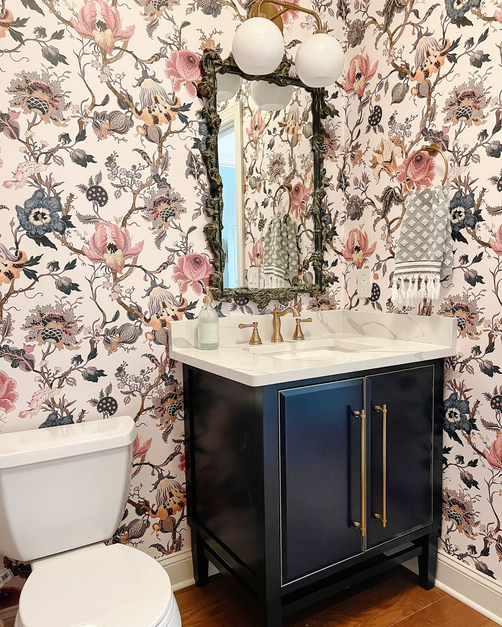 Proof that small spaces can make the biggest statement 💙✨ We turned this half bath into a true jewel box moment with dramatic botanical wallpaper, a grounding navy vanity, and warm brass accents for contrast and glow. A crisp white quartz top keeps it fresh, while a sculptural mirror and soft lighting elevate the entire experience. Don’t play it safe — lean into personality. Shop a similar bold bath look below. 

 #LTKHome