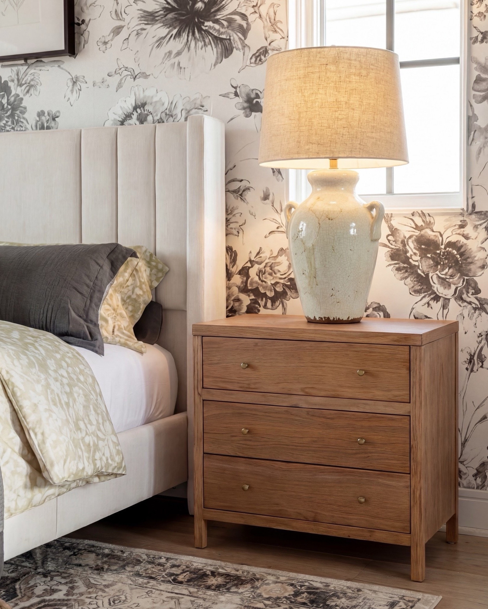 Shop the look:
• Upholstered channel-tufted bed — ivory/cream
• Chunky knit throw — warm chestnut brown
• Decorative pillows — muted sage, oatmeal, charcoal
• Light oak nightstands — natural finish
• Ceramic table lamps — soft cream
• Woven ottomans — natural jute
• Patterned area rug — taupe, sand, charcoal
• Accent chair — cream upholstery with warm wood frame
• Botanical wall art — black frames
• Floral wallpaper — charcoal sketch on ivory background

#LTKhome #LTKsale #LTKstyletip