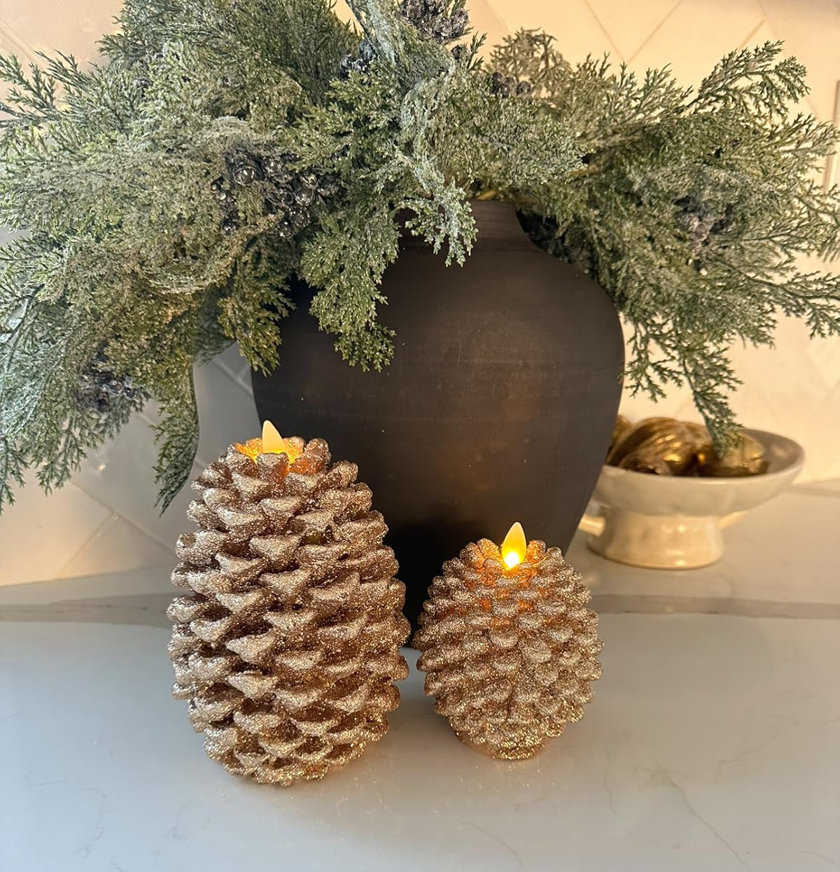 Holiday kitchen vignette. Pine stems with berries, black organic vase, gold figs, white pedestal bowl, flameless pinecone candles. | Amazon (US)