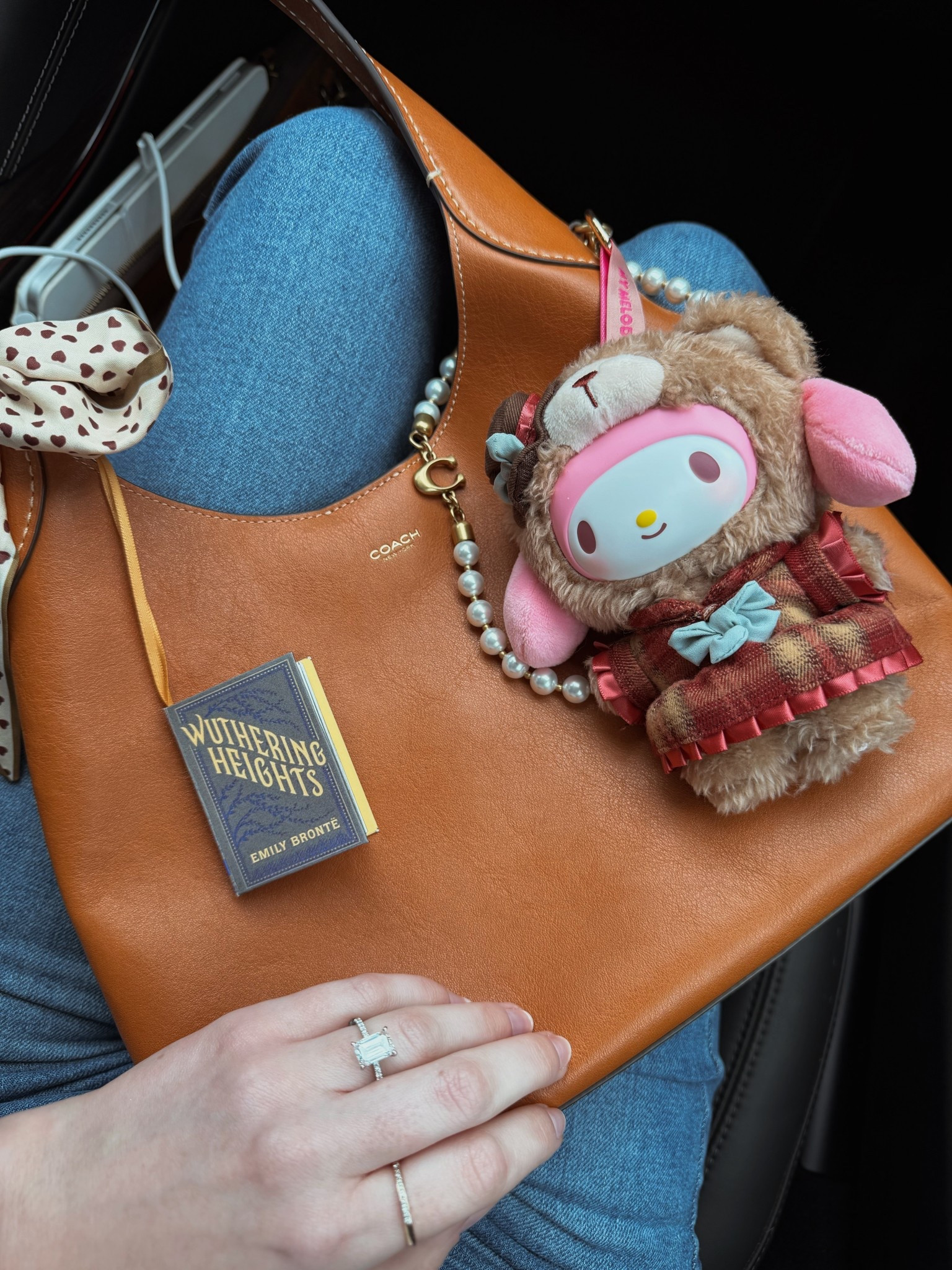 Bag of the day 🤎 I’m loving the mini book ornaments I’ve been buying to use as bag charms since the Coach mini books have been impossible to get!

Coach Brooklyn 28 in the color toffee
Coach pearl strap connector
Twilly
Hello kitty tea room blind box
Wuthering heights book ornament / book bag charm