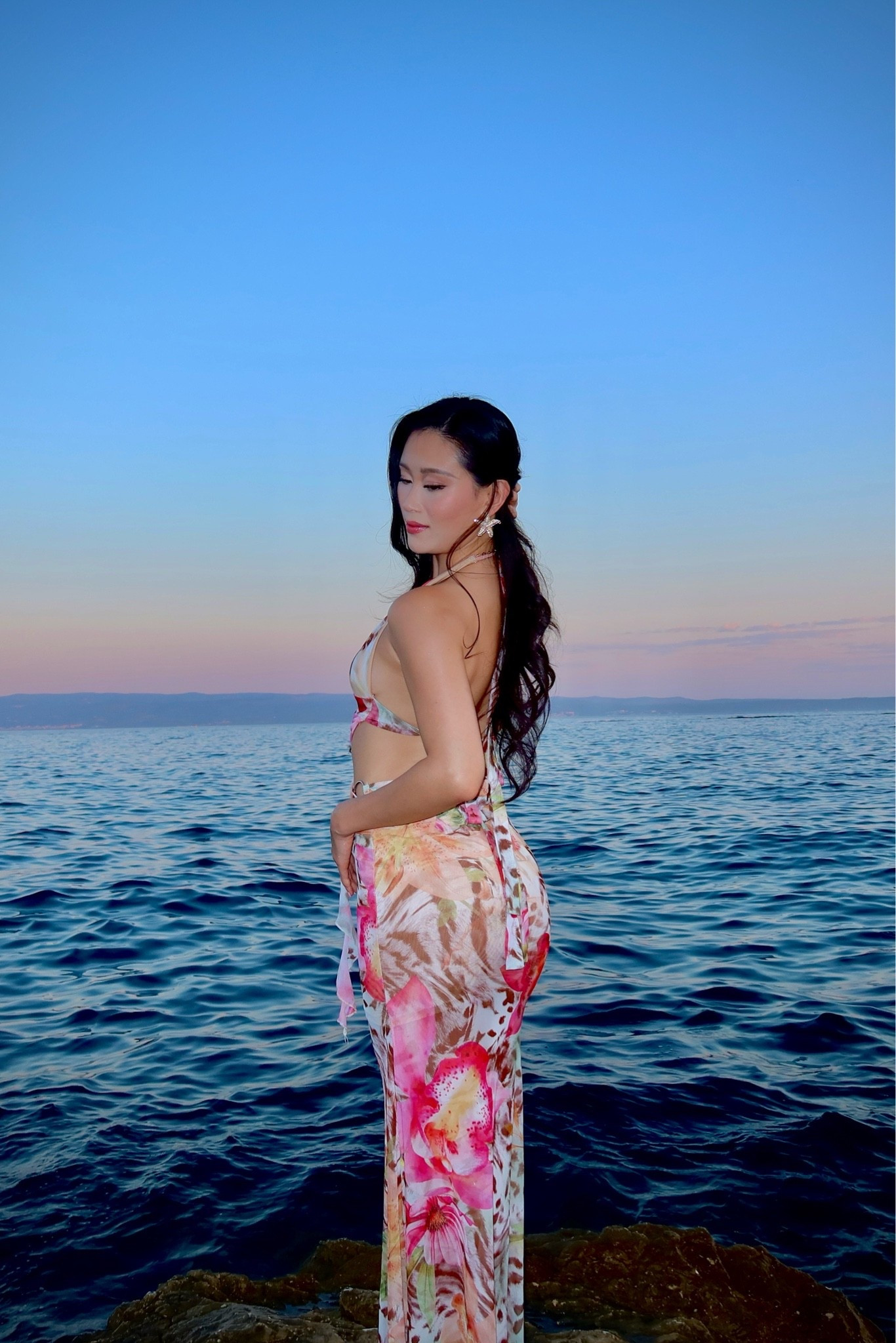 a tropical floral print maxi dress with a halter neckline, plunging open back, and figure-skimming silhouette in pink lily and leopard print on a cream base, styled with crystal starfish statement earrings for golden hour on the dalmatian coast. the bold tropical floral print and sultry open-back silhouette make this the ultimate statement resort dress for sunset evenings by the water. perfect for croatia sunsets, hvar beach club nights, dalmatian coast vacations, and mediterranean resort evenings. shop this look linked above.
