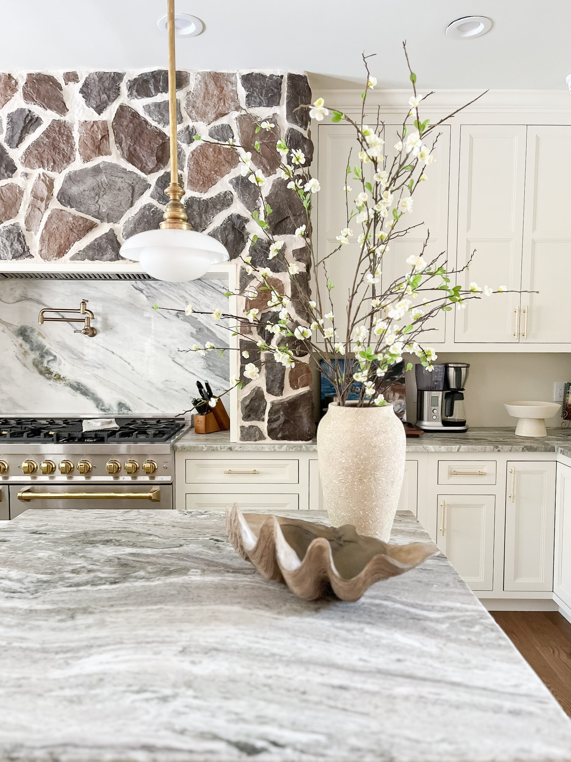 Open sightlines, layered texture, and timeless finishes ✨ Removing the wall completely transformed the energy of this home, and that stone range hood steals the show. Soft-veined quartz with a full-height slab backsplash keeps everything feeling seamless, while ceiling-height cabinetry, classic pendants, and upgraded appliances bring a modern polish that still feels warm and livable. Shop a similar look for your own kitchen refresh below. 🤍 

 #LTKHome