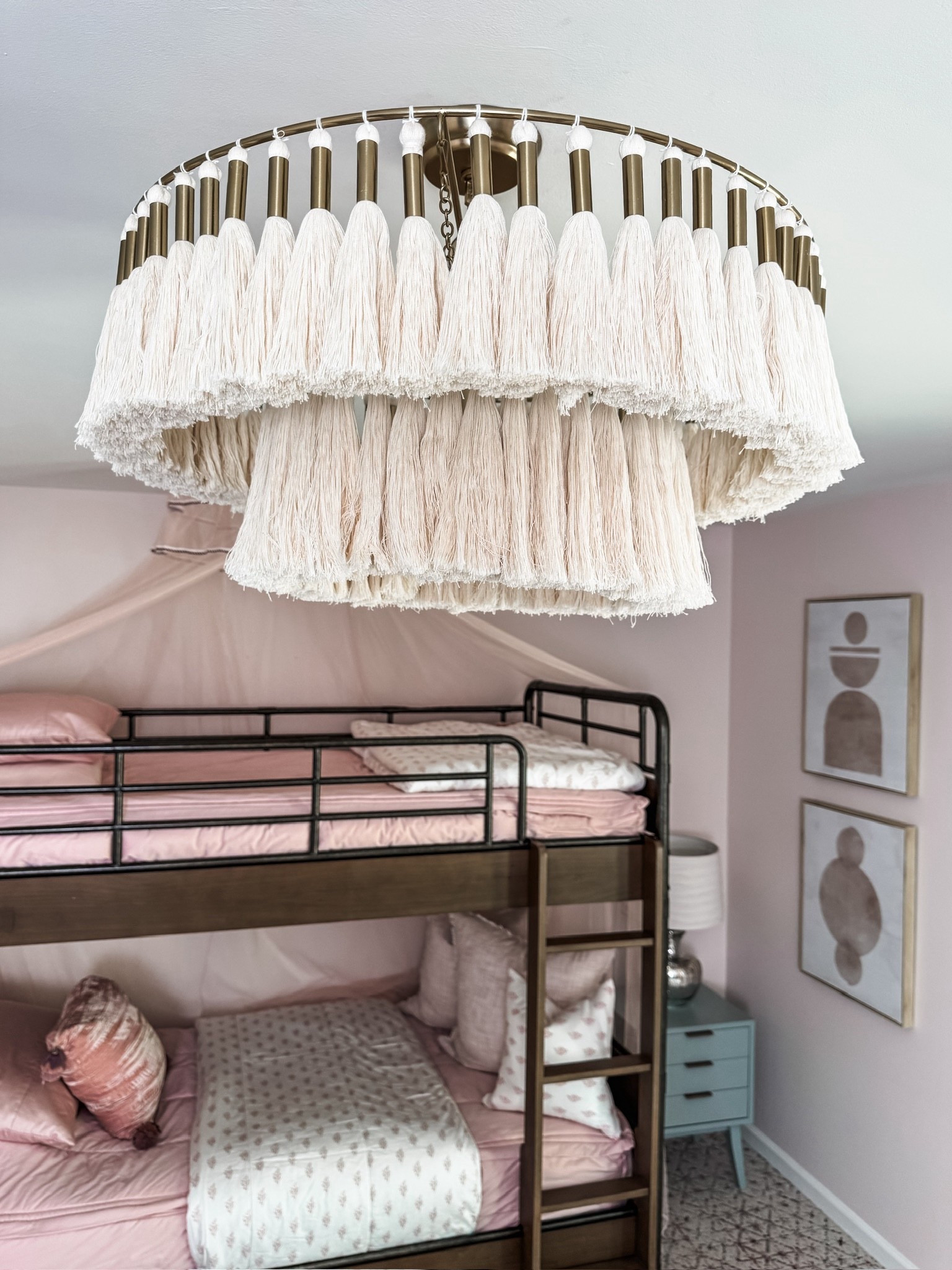 A dreamy kids’ bedroom ✨ This space features a wooden bunk bed layered with pink bedding and plush throw pillows, topped with a romantic canopy. The tassel chandelier adds texture overhead, while modern side tables with lamps and soft curtains frame the room. A cozy accent chair with heart and patterned pillows, framed wall art, and a patterned carpet by FLOR complete the look. 🌸

Girls: 
Alexandria Luxe Beddy’s (Twin, Minky, ZipBase)
Eden Blanket 
Ella Medium Pillow Cover 
Ella Pillowcase 
Ella Sham 
Eden Euro Pillow Cover 

#KidsRoomDesign #BunkBedStyle #PinkBedding #ThrowPillows #CanopyBed #TasselChandelier #SideTables #TableLamps #WallArt #AccentChair #PatternedRug #eanesinteriors

#LTKHome #LTKOver40 #LTKStyleTip