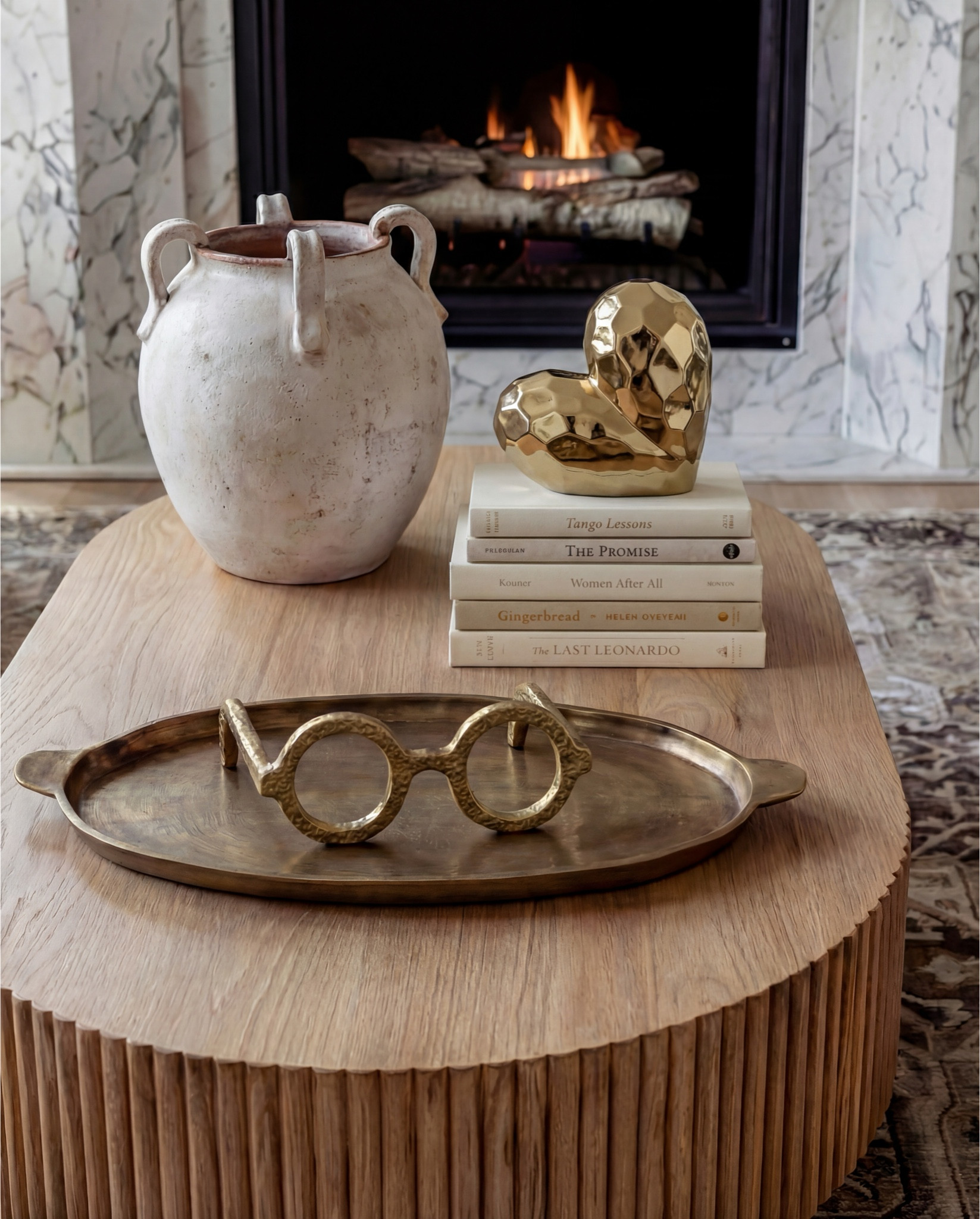 Shop the Look:
• White upholstered sofa (clean-lined, low profile)
• White upholstered armchairs (pair)
• Light wood round coffee table (fluted or ribbed base)
• Neutral vintage-style area rug (muted brown and beige tones)
• Marble fireplace surround
• Black fireplace insert
• Large framed landscape wall art (soft blue and neutral tones)
• Brass wall sconces (pair, globe style)
• White globe pendant light with brass detail
• Natural wood ceiling beams
• Light wood flooring

Coffee Table Styling:
• Large white ceramic vase (rustic sculptural style)
• Decorative hardcover books (neutral covers)
• Gold abstract heart sculpture
• Brass oval tray
• Decorative brass object (sculptural accent)

Sofa Styling:
• Neutral throw pillows (warm beige)
• Chunky knit throw blanket (camel or warm brown)

Media Console Area:
• Light wood sideboard / media console (carved front detail)
• Brass cabinet knobs
• Black figurine sculptures (musician figures, set of three)
• Brown ceramic vase
• Dried branches / minimalist floral stems
• Brass decorative tray

#LTKHome #LTKFindsUnder100 #LTKSaleAlert