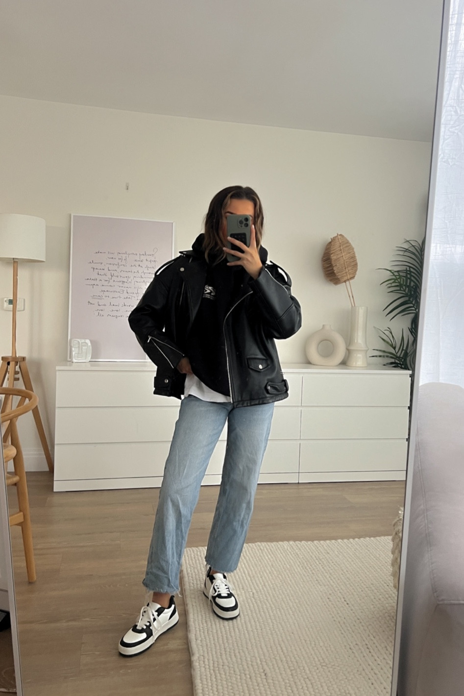 Ways to style a leather jacket - teaming blue straight leg jeans with black and white trainers for a comfy everyday look 