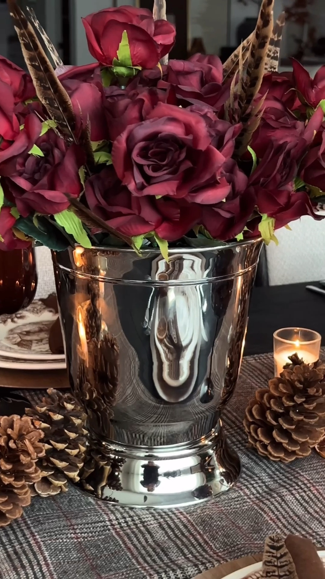 Ralph Lauren inspired tablescape, Ralph Lauren lodge aesthetic, moody fall table decor, fall hosting, autumn tablescape, plaid table runner, brown transferware dishes, stag plates, woodland dinnerware, wood chargers, chocolate brown cloth napkins, silver napkin rings, feather napkin accents, burgundy roses, silver centerpiece vase, brown stemmed glasses, silver flatware, taper candles, mixed height candle holders, votive candles, layered candlelight, pinecone table decor, dried orange slices, rustic elegant table setting, cozy candlelit dinner, Thanksgiving table inspiration, collected table style