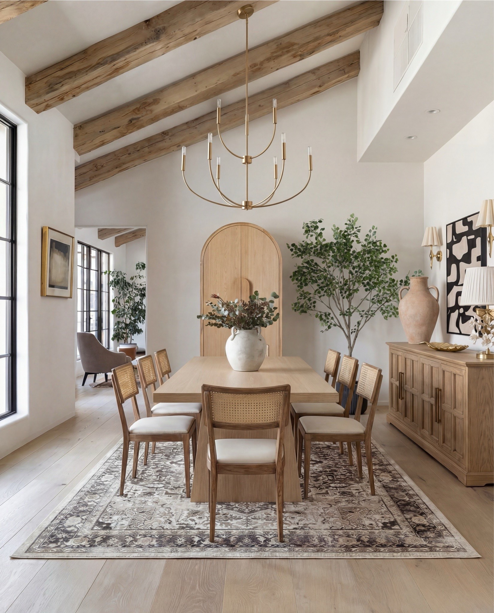 This dining room feels warm, sculptural, and effortlessly refined. Natural wood tones and woven textures bring softness to the space, while the oversized chandelier and arched details add quiet architectural drama. The neutral palette keeps everything calm and elevated, letting the organic shapes and materials feel timeless rather than trendy.

The styling is minimal yet layered—light oak finishes, cane-back seating, soft textiles, and subtle brass accents that create a relaxed, modern-traditional atmosphere.

Shop the Look:
• Light oak rectangular dining table
• Cane-back wood dining chairs with neutral seat cushions
• Neutral vintage-style area rug (taupe + brown tones)
• Brass modern chandelier with curved arms
• Large ceramic vase with greenery stems
• Wood sideboard buffet cabinet (natural oak finish)
• Textured ceramic floor vase (warm beige)
• Brass wall sconces with tapered shades
• Abstract neutral wall art (black + cream tones)
• Wood arched cabinet or pantry storage
• Neutral linen table styling accessories
•Brass hurricane candle holders 
•brass tray
•Modern wall art
Faux tree
•Black tree planter
•Brass decorative  table all 
Brass decor tray and bowl
•Runner rug

#LTKSaleAlert #LTKHome