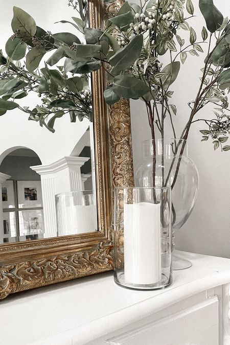 Mantle styling 
Faux stems 
Glass Hurricane 
White pillar candle 
Gold antique mirror 

#LTKstyletip #LTKFind #LTKhome