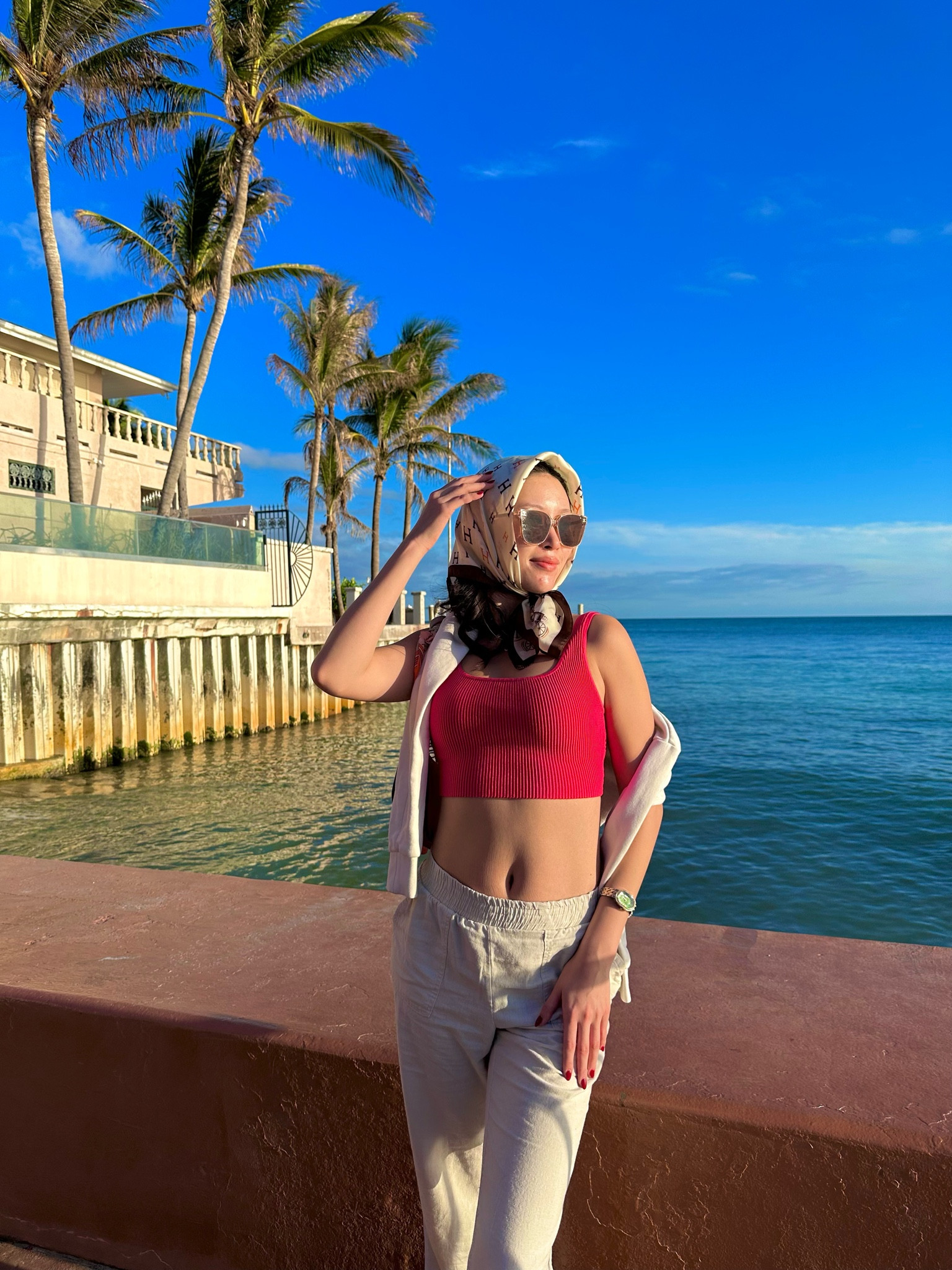 a hot pink ribbed knit crop tank styled with cream linen pants, a white sweatshirt tied over the shoulders, a designer silk monogram headscarf, rose-tinted oversized sunglasses, gold watch, and red nails for a coastal walk in palm beach. the polished mix of preppy separates and signature silk scarf styling makes this the ultimate young old money palm beach outfit. perfect for palm beach trips, worth avenue shopping, coastal preppy vacations, and quiet luxury vacation styling. shop this look linked above.

#LTKootd