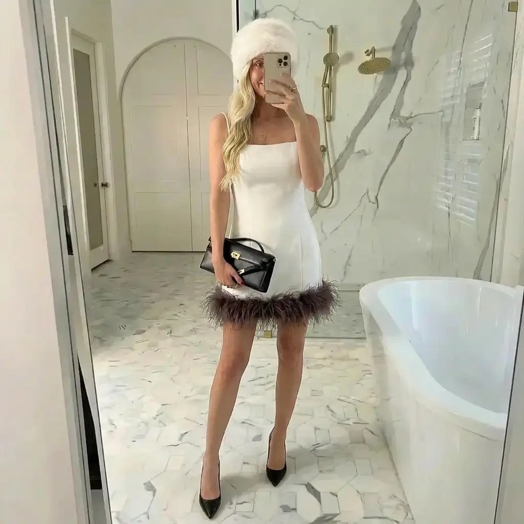 A polished mirror selfie in a bright marble luxury bathroom with soft, natural lighting. A tall, elegant blonde woman wears a fitted white mini dress with a feather-trim hem, paired with sleek black pointed-toe heels and a structured black designer clutch. She completes the look with a fluffy white winter hat, adding a playful yet refined cold-weather accent. Her hair falls in loose, glossy waves, and the overall aesthetic feels modern, feminine, and quietly glamorous — a blend of winter chic, old-money elegance, and effortless confidence.

⸻

HASHTAGS

#WinterChic
#QuietLuxury
#FeatherTrim
#WhiteDressMoment
#OldMoneyAesthetic
#ColdWeatherStyle
#LuxuryAesthetic
#FeminineEnergy
#SoftGlam
#ChicMinimalism
#MirrorOutfit
#ElegantStyle
#WinterGlam
#TimelessFashion
#ModernRomantic
#OOTD
#MainCharacterMoment
#NeutralLuxury
#StatementLook
#ClassicWithATwist

#LTKdayinmylife #LTKGiftGuide #LTKHoliday