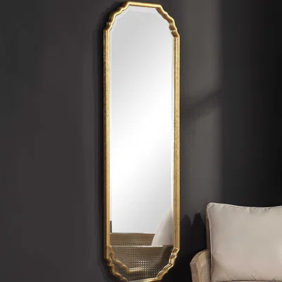 tall gold leaf wall mirror with curved frame leaning against a wall
