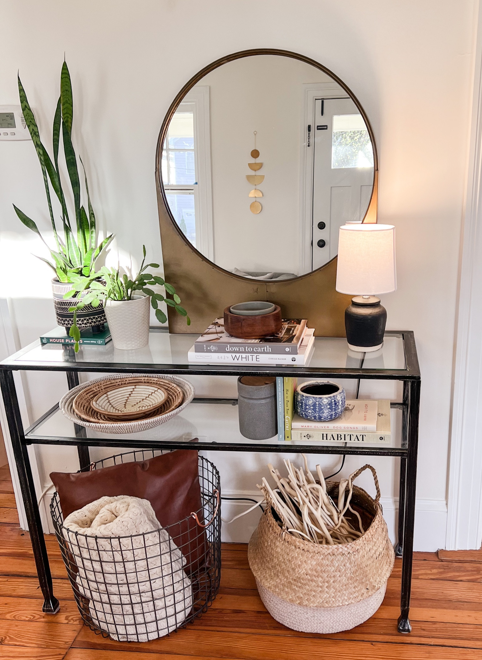 Front table console with lots of neutral tones and natural elements: gold round mirror (this one is vintage from Holistic Habitat!), plants, woven baskets, books, belly basket, and other smaller decor items. The wall hanging in the reflection is a beautiful, reflective piece from The Citizenry. These decor books make great gifts for friends who love design. 

#LTKFind #LTKGiftGuide #LTKhome