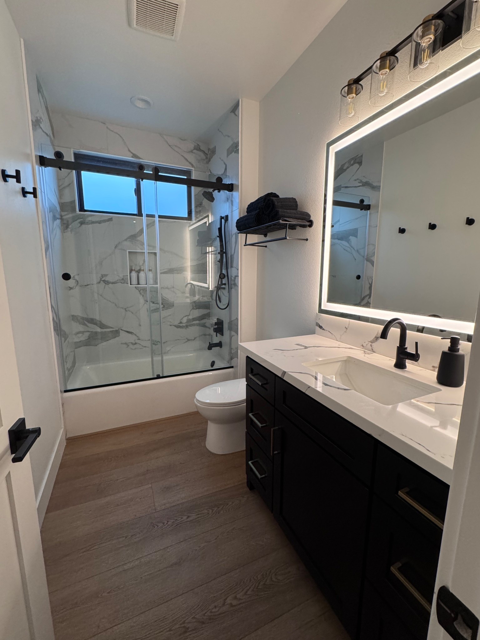 Guest bathroom | black cabinets | faucet | glass shower door | wood floors | towel rack | bath towel | soap dispenser 

#LTKU #LTKHome #LTKSeasonal