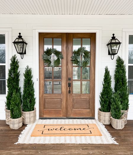Front porch decor faux artificial cedar trees emerald green arborvitae basket planters double layered doormat and jute, scatter rug, front door and front porch styling wreaths, outdoor wall sconces, lantern lighting modern farmhouse style

#LTKhome #LTKFind #LTKSeasonal