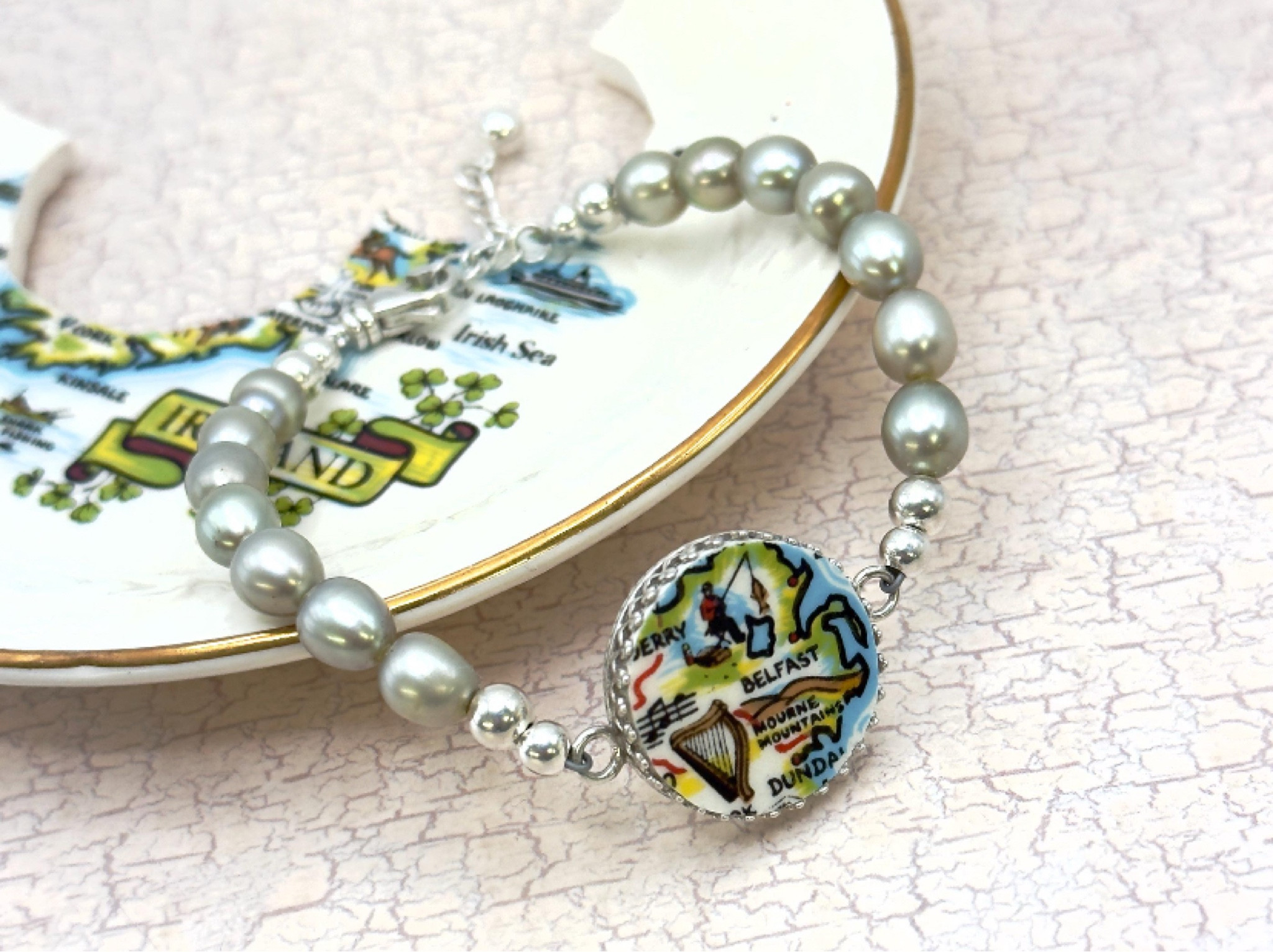 Carry a little bit of Ireland with you! This handmade Irish broken china bracelet features a vintage map of Ireland, set in sterling silver, and highlighting Belfast, the Mourne Mountains and surrounding areas. Strung with luminous light sage green freshwater pearls, this bracelet exudes an elegant yet nostalgic charm - perfect for lovers of Irish heritage and travel. #oneofakind #uniquejewelry #belfast #ireland 

#LTKMostLoved #LTKU #LTKTravel
