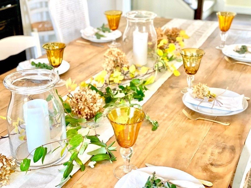Simple Easy Thanksgiving tablescspe in neutral, gold and green! Neutral runner, glass hurricane candle holders, white dinner plates, gold goblets, white napkins and gold flatware. 

Tip- cut dried flowers from garden to create a centerpiece. #thanksgivingtable #neutraltablescape #thanksgiving 

#LTKHoliday #LTKHome