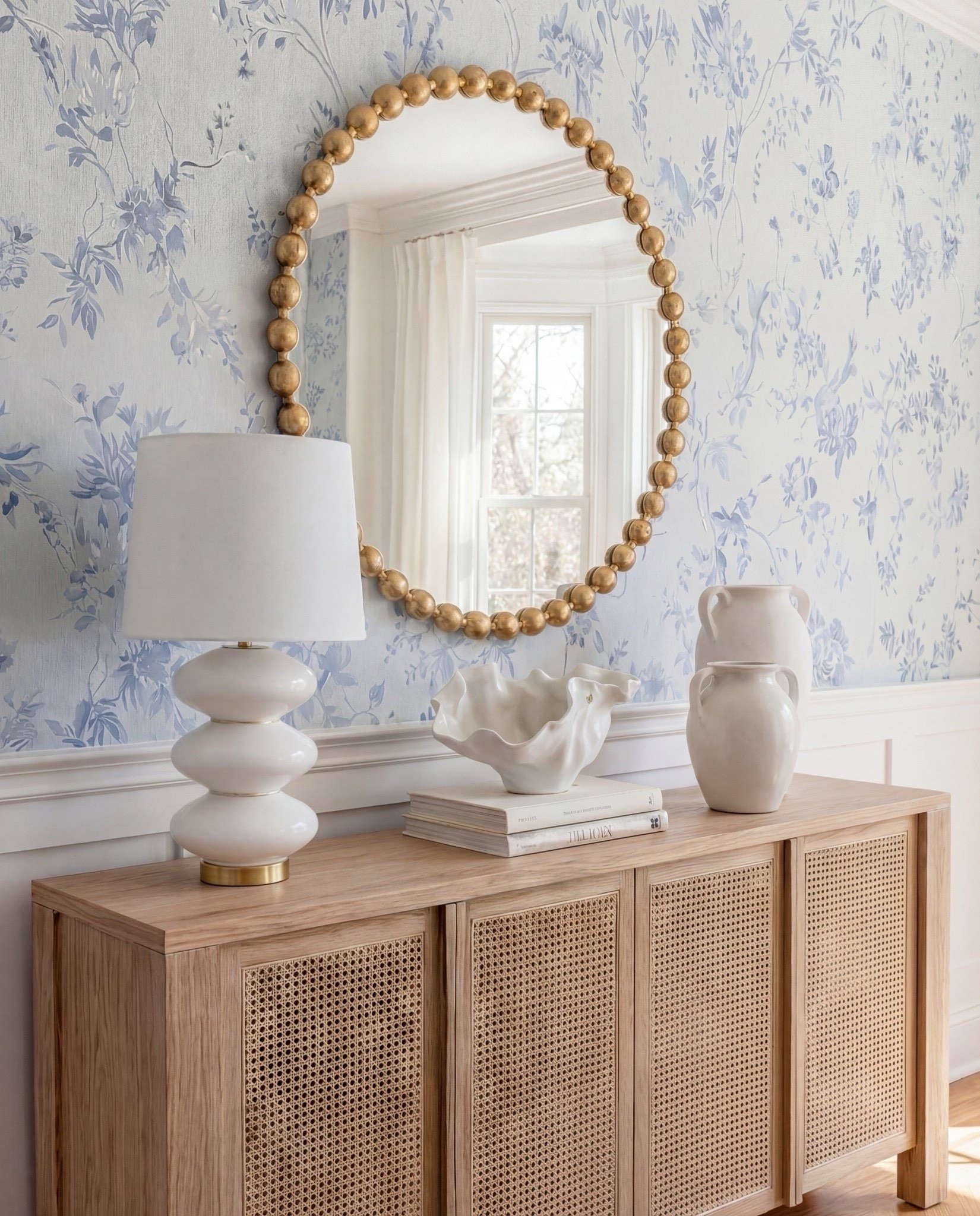 A bright and inviting dining room layered with soft blues, warm wood tones, and sculptural textures. The fluted pedestal table and cane buffet bring in organic warmth, while the cream upholstered chairs add a clean, modern softness. The floral wallpaper and vintage-style rug tie the whole palette together—light, airy, and effortlessly elevated.

✨ Shop the Look:
• Light oak fluted pedestal dining table
• Cream textured upholstered dining chairs with brass base
• Cane-front light oak sideboard
• Sculptural white stacked ceramic table lamp
• Oversized round brass ball mirror
• Matte white ceramic vases
• Glass hurricane candle holders
• Blue & taupe vintage-style rug
• Soft blue floral wallpaper

#LTKSaleAlert #LTKHome