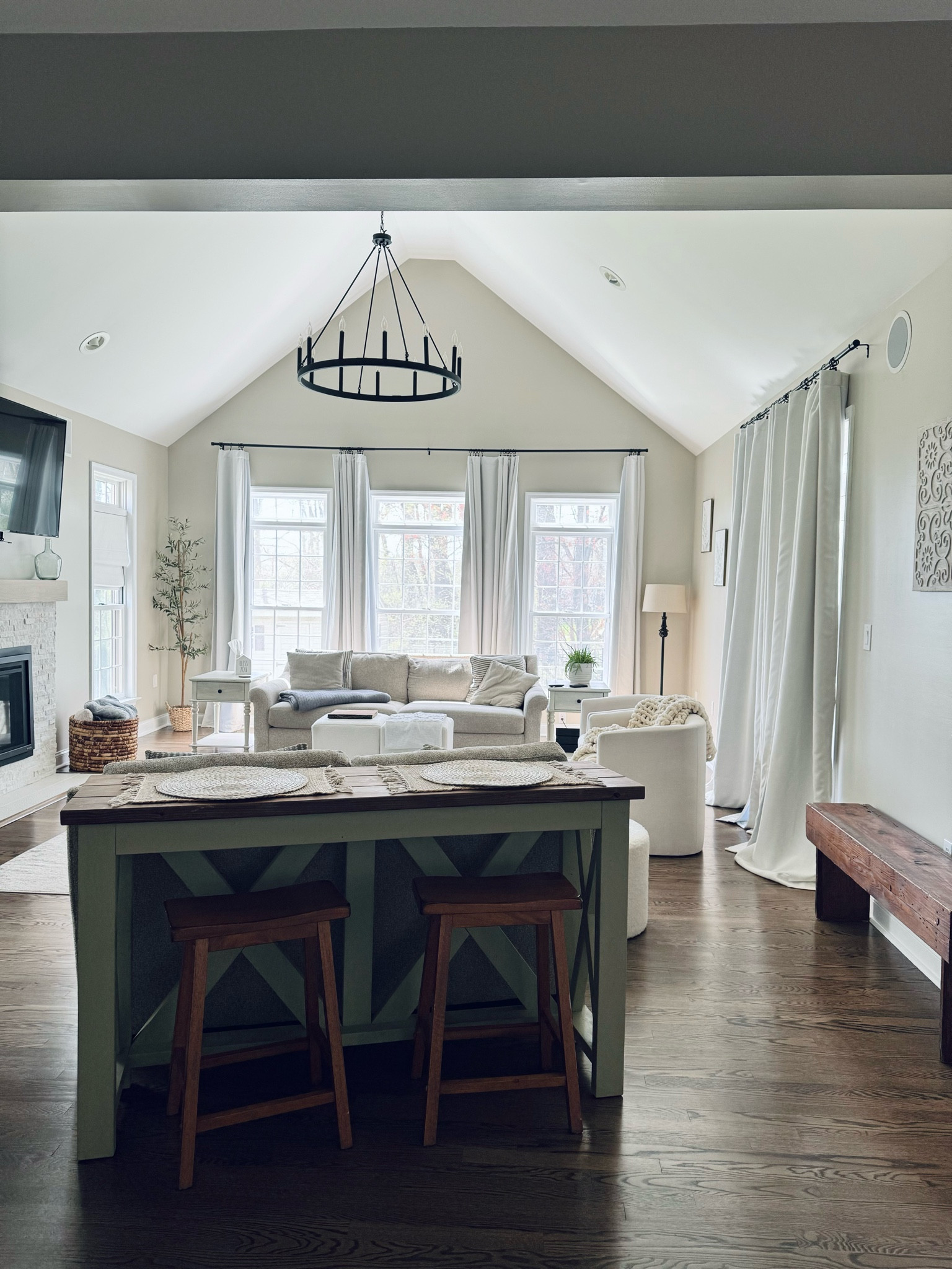 Neutral living room 🤍
We had hard wood flooring installed in this room, replaced the very dated chandelier, painted the walls “Accessible Beige” by Sherwin Williams. We also tiled over the brick fireplace to give it a fresh look!

This room boasts a lot of sentimental items:
My dad built the two seated sofa table, and I painted & stained it. 
The bench was built by my grandfather and I inherited it when he passed. 
The basket on the floor was my grandmothers, which I also inherited when she passed. 