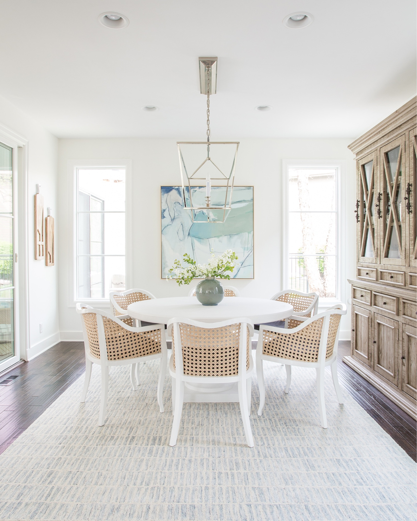 Our prior neutral dining room with a blue and white modern rug, round white dining table, cane dining chairs, blue and green abstract art, a linear chandelier and faux greenery. Items not shown include a distressed wood buffet, a cake stand, marble coasters and a rectangular wall mirror. 

spring dining room, blue and white decor, neutral decor, Serena and Lily dining room, dining room table, dining room chairs, dining room rug, area rugs #ltkhome #ltkseasonal #ltksalealert #ltkunder50 #ltkstyletip #ltkunder100 #ltkfind 

#LTKfamily #LTKSale #LTKstyletip #LTKunder100