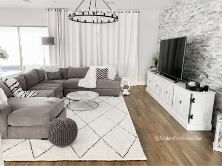 Living room furniture and rug at Modern Farmhouse Glam. Neutral area rug, white diamond rug, white and gray rug, gray sectional sofa couch, wagon wheel iron lighting fixture Chandelier, white 120 inch curtains, media console table, floor lamp, ottoman, marble coffee table, pouf. 

#LTKhome