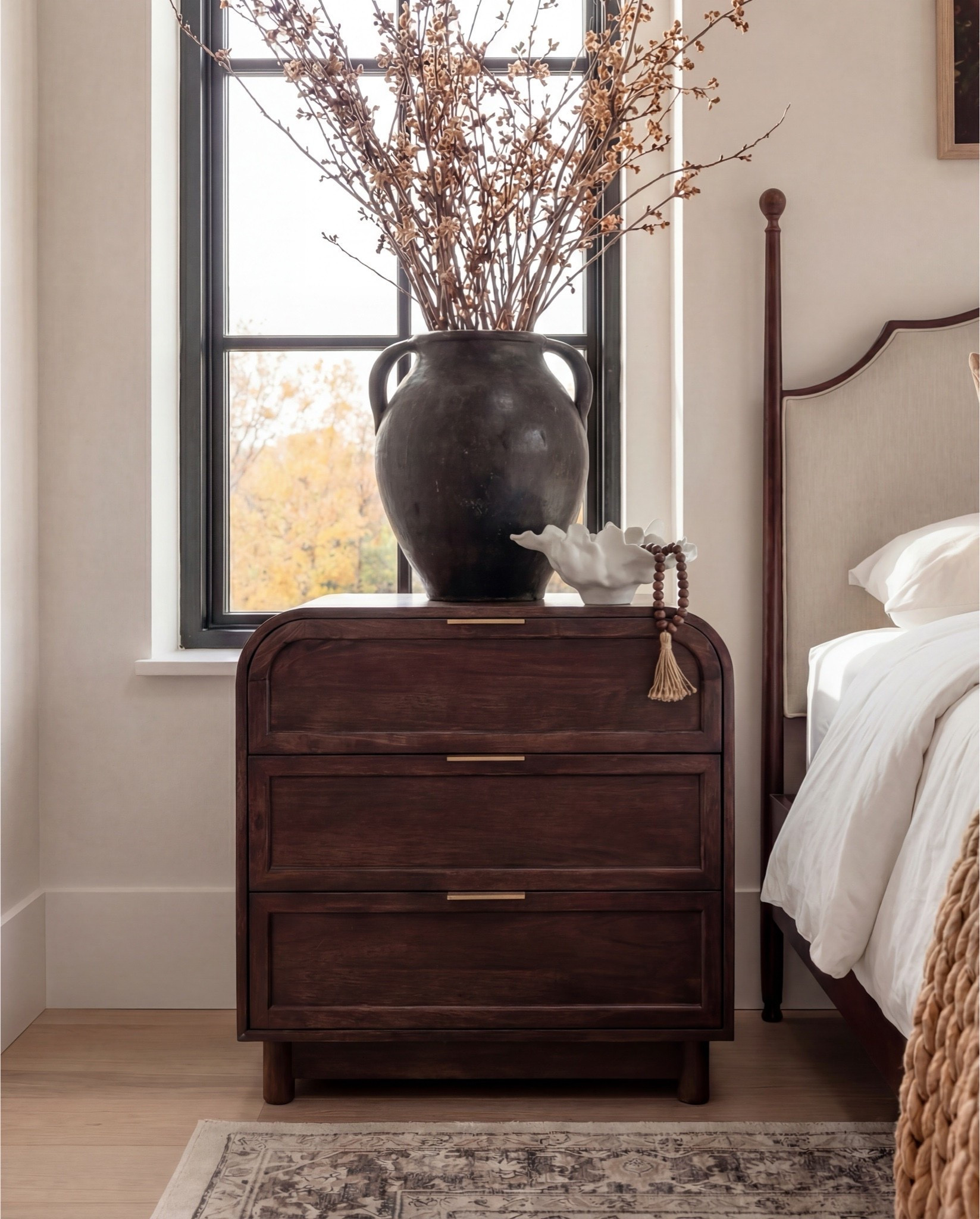 This bedroom balances classic craftsmanship with a clean, modern layout. Warm wood tones, soft textiles, and sculptural accents create a calm, elevated feel that feels timeless but not heavy.

Shop the Look: Bedroom Refresh
Furniture & Decor
	•	Upholstered wood bed frame (cream fabric)
	•	White bedding set
	•	Chunky knit throw (camel)
	•	Patterned accent pillows (rust/brown)
	•	Wood nightstands
	•	Ceramic table lamps (black base, white shade)
	•	Curved brass-framed wall mirror
	•	Framed floral wall art above bed
	•	Upholstered boucle bench stools (set of two)
	•	Vintage-style area rug (neutral pattern)
	•	Wood dresser with brass corner details
	•	Decorative ceramic vase
	•	Stacked neutral books
	•	Brass decorative tray
	•	Sculptural brass object
	•	Framed artwork above dresser
	•	Exposed wood ceiling beams

#LTKFindsUnder100 

#LTKSaleAlert

#LTKhome #LTKsale