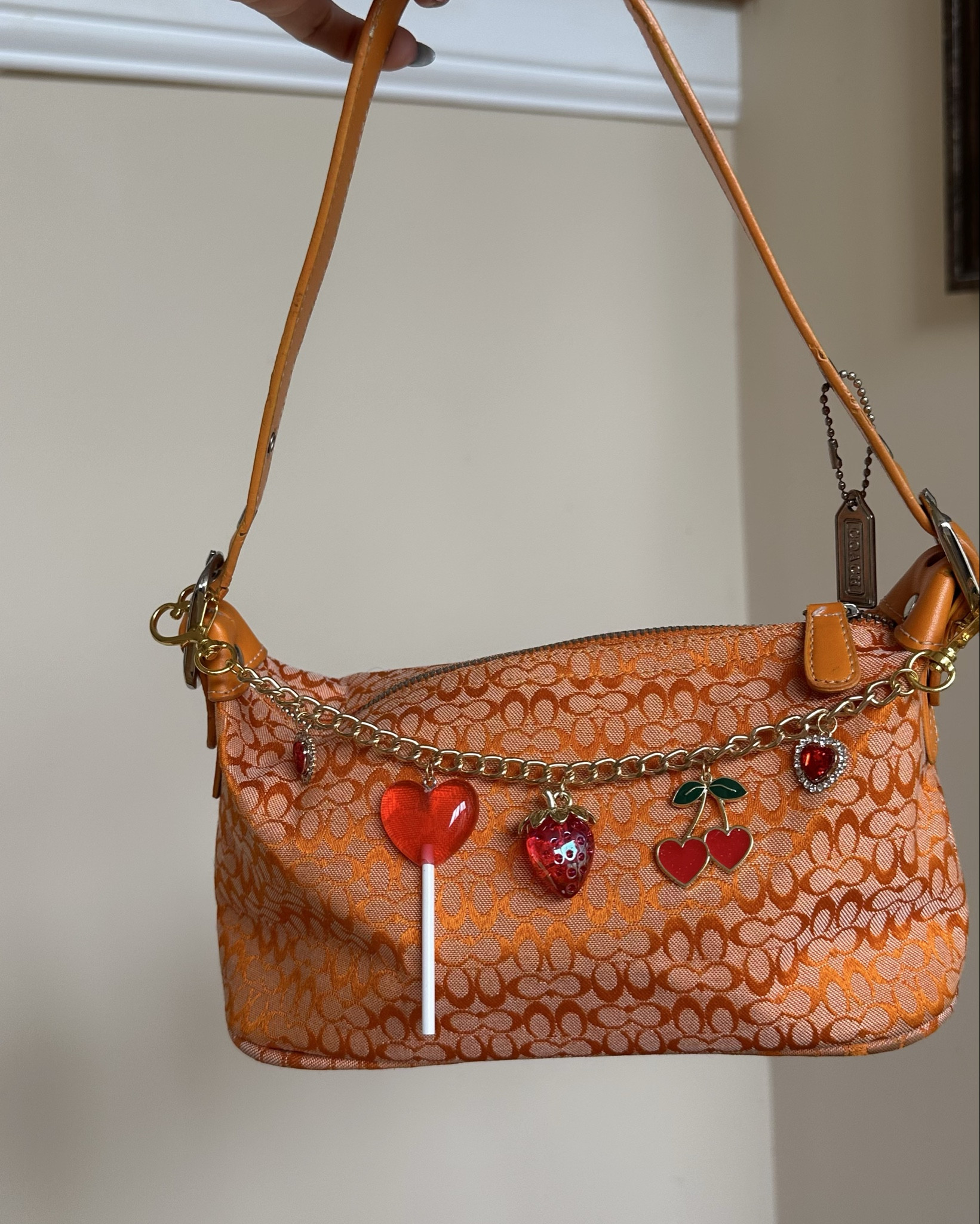 Stylish orange patterned shoulder bag featuring playful charms. Perfect for adding a pop of color to any outfit. 

Please note: This purse is NOT an authentic Coach product. It is a replica/inspired design made to look similar in style but is not affiliated with, endorsed by, or manufactured by Coach.

Charm included.

All sales final. Smoke free home.
