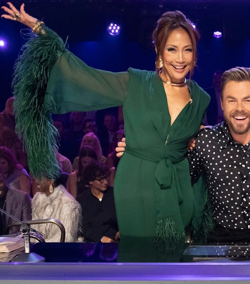 Carrie Ann Inaba wearing a green Maxi Dress features a chiffon fabric with a front slit and feather embellishments at the cuffs. It is partially lined with padding at the shoulders. It has a hidden back zipper closure and a front hook and eye closure at the neckline on Dancing With the Stars