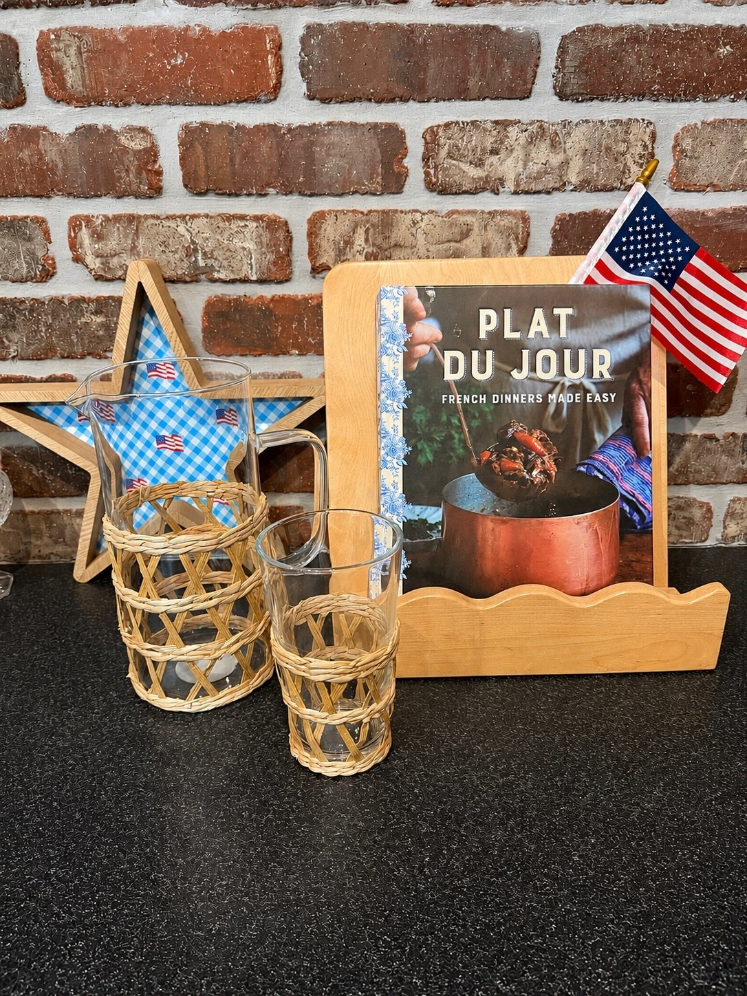 Patriotic Kitchen Finds I’m Loving 🇺🇸✨

A few of my favorite kitchen and tabletop finds styled together! This charming setup combines natural woven textures, classic wood accents, and festive patriotic touches that work beautifully from Memorial Day through summer entertaining. The scalloped cookbook stand, blue gingham star décor, woven glassware, and French-inspired cookbook create the perfect blend of cozy cottage and coastal charm. ❤️🤍💙

#ltkhome #patriotichomedecor #summerdecor #coastaldecor #kitchenstyling #amazonhomefinds #tablescapedecor #chinoiseriestyle #preppyhome #americanstylehome

#LTKHome #LTKfoodie #LTKSeasonal