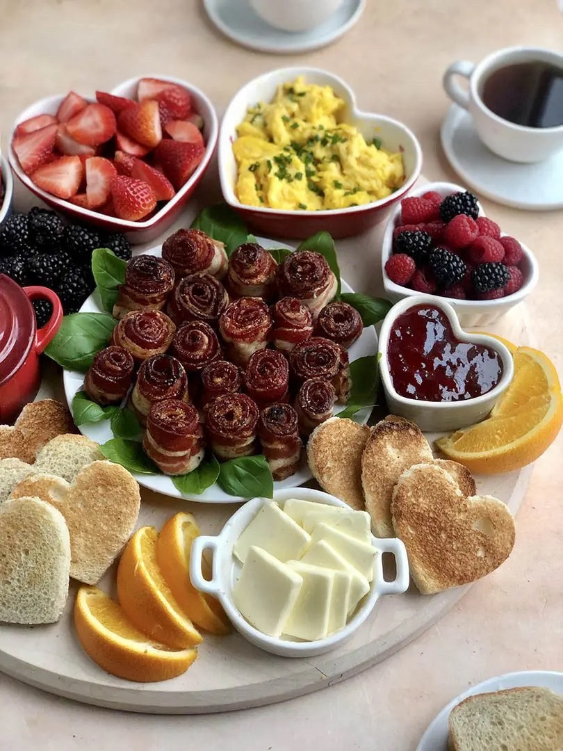 
Ingredients
BACON BOUQUET
* 12 slices Bacon (24 for double roses)
* 2 tbsp Maple syrup
* 1 tbsp Brown sugar
* 1 tsp Black pepper
* 1 bunch Basil leaves
BACON ROSE BRUNCH BOARD INGREDIENTS 
* 12 Bacon Roses
* 10-12 Eggs scrambled
* 10-12 slices Bread
* 1/2 cup Butter sliced
* 1/2 cup Jam
* 16 oz Strawberries
* 8 oz Blackberries
* 8 oz Raspberries
* 4 oz Pomegranate Seeds
* 2 Oranges, sliced
* 1 tbsp Chives chopped
* 2 tbsp Parmigiano Reggiano grated


Instructions 
* Preheat oven to 400 degrees  
* Take a strip of bacon, and starting at one end, roll it up tightly to form a rosette. Feel free to add another bacon strip layer for an even heftier looking rose. 
* Secure the bacon rose with two toothpicks to form a cross (as close to the bottom of one end as you can) 
* Space out the bacon roses on a wire rack on top of a foil lined baking sheet Brush bacon roses with maple syrup then sprinkle brown sugar and cracked black pepper 
* Bake until bacon is cooked all the way through, 20-30 minutes (40 for double-layered roses). Feel free to turn over or finish them off in a frying pan if needed. 
* Set aside and let cool; remove toothpicks. 
* Arrange bacon roses on a round salad platter to form a “bouquet” and place it in the center of your serving board. Place basil leaves under each bacon rose around the outside of the bouquet. 
* Next, start adding ingredients in small bowls around the edge of your round board. Use the bigger bowls for fruit like berries and the smaller ramekins for jam and small scale fruit like pomegranate seeds. You can also lay some fruit directly onto the board. 
* Add your warm ingredients like eggs last. I did one batch with chives on top and one with Parmigiano Reggiano. I generally like to have dairy and non-dairy options available. 
* Cut bread using a heart-shaped cookie cutter and toast. Serve and enjoy! 


#LTKSeasonal #LTKfoodie