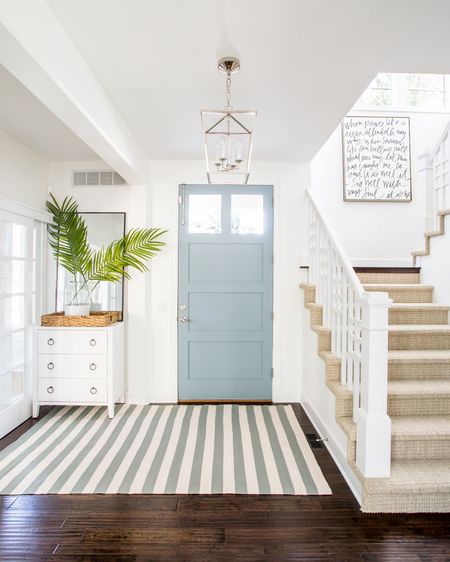 Our Omaha entryway decorated for summer with a white glossy raffia cabinet, blue and cream striped rug, lantern pendant light, “It Is Well” canvas art, tall thin black framed mirror, faux palm leaves and a paint dipped vase.

#ltkhome #ltkseasonal #ltkstyletip #ltkfindsunder50 #ltkunder100  coastal decorating, foyer ideas, blue and white decor

#LTKhome #LTKSeasonal #LTKsalealert