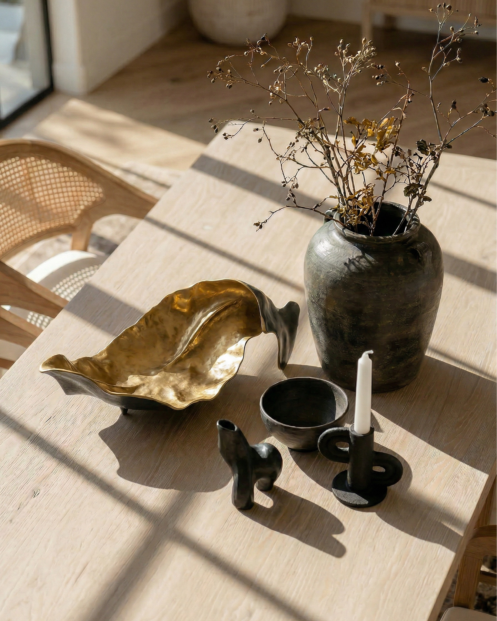 * Rectangular light wood dining table (traditional trestle base)
* Woven cane dining chairs (natural oak frame)
* Neutral vintage-style area rug (distressed pattern)
* Brass modern chandelier (linear / sculptural arms)
* Rustic exposed wood ceiling beams (reclaimed look)
* Large black-framed sliding glass doors (industrial style)
* Dark ceramic vase (handmade / organic texture)
* Dried floral arrangement (neutral stems)
* Sculptural brass decorative bowl
* Black ceramic candle holder (modern abstract form)
* White taper candle
* Small matte black decorative bowl
* Minimalist sculptural object (black accent piece)
* Light wood sideboard cabinet (fluted / ribbed detailing)
* Built-in arched niche cabinet (custom millwork look)
* Decorative pottery (neutral ceramic vases)
* Framed landscape wall art (classic / muted tones)
* Indoor olive tree (or faux olive tree)
* Neutral linen / textured textiles
* Warm light oak flooring
* Soft cream / off-white wall paint
* Arched doorway architectural detail

#LTKHome #LTKSaleAlert