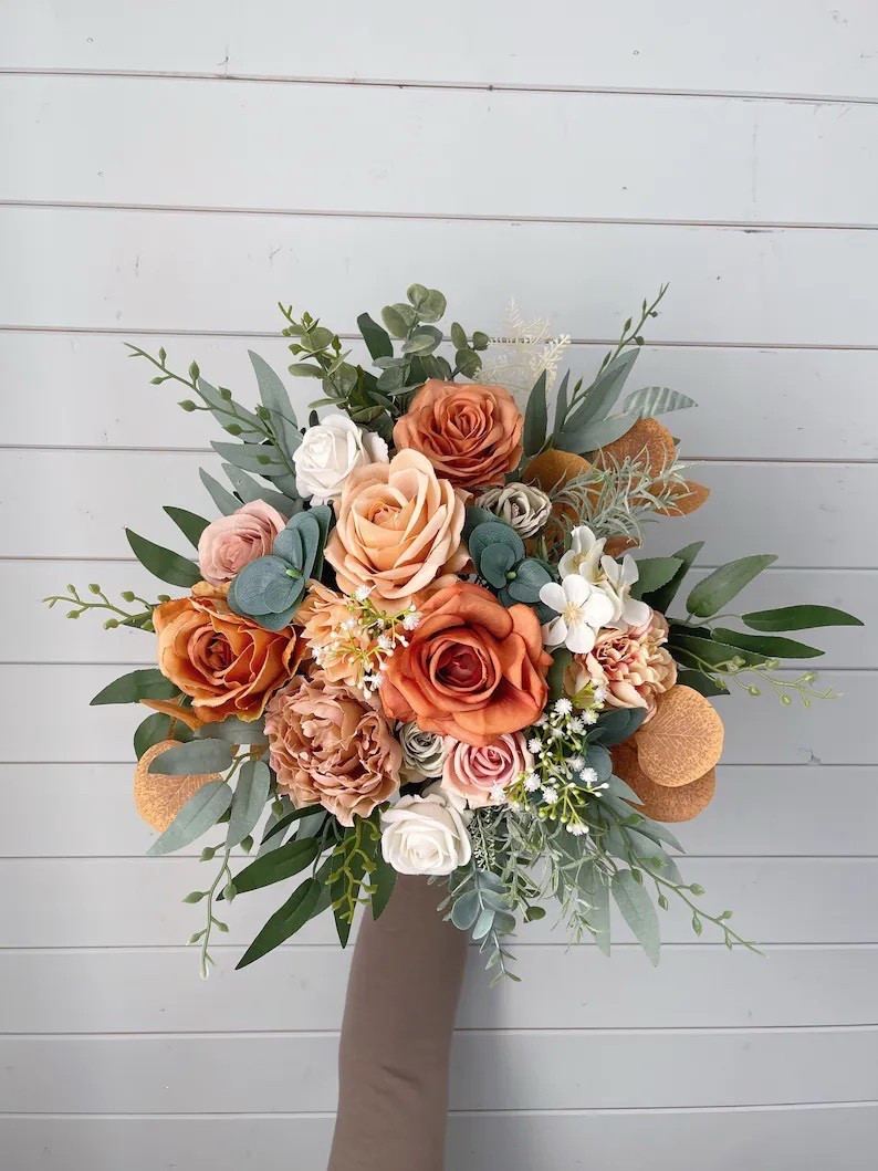 This terracotta bridal bouquet is a stunning blend of warm, earthy tones and timeless romance. Designed with lifelike silk flowers in shades of burnt orange, champagne, ivory, and soft greenery, it creates a rich autumn-inspired palette that looks beautiful in photos and lasts long after the celebration. The satin ribbon-wrapped handle adds a classic finishing touch, making this bouquet a perfect choice for fall weddings, rustic ceremonies, or boho-inspired bridal looks. #LTKwedding #bridalbouquet #fallwedding #bohowedding #weddinginspiration #rusticwedding #bridetobe #weddingflowers #silkflowers #weddingstyle

#LTKHome #LTKWedding #LTKSeasonal