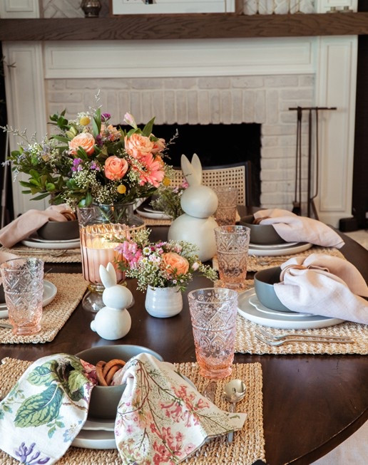 Easter table setting featuring floral printed napkins, woven place mats, green bowls, colored glassware, bunnies, and a floral arrangement in a rattan wrapped vase. 

#LTKFindsUnder50 #LTKHome #LTKSeasonal