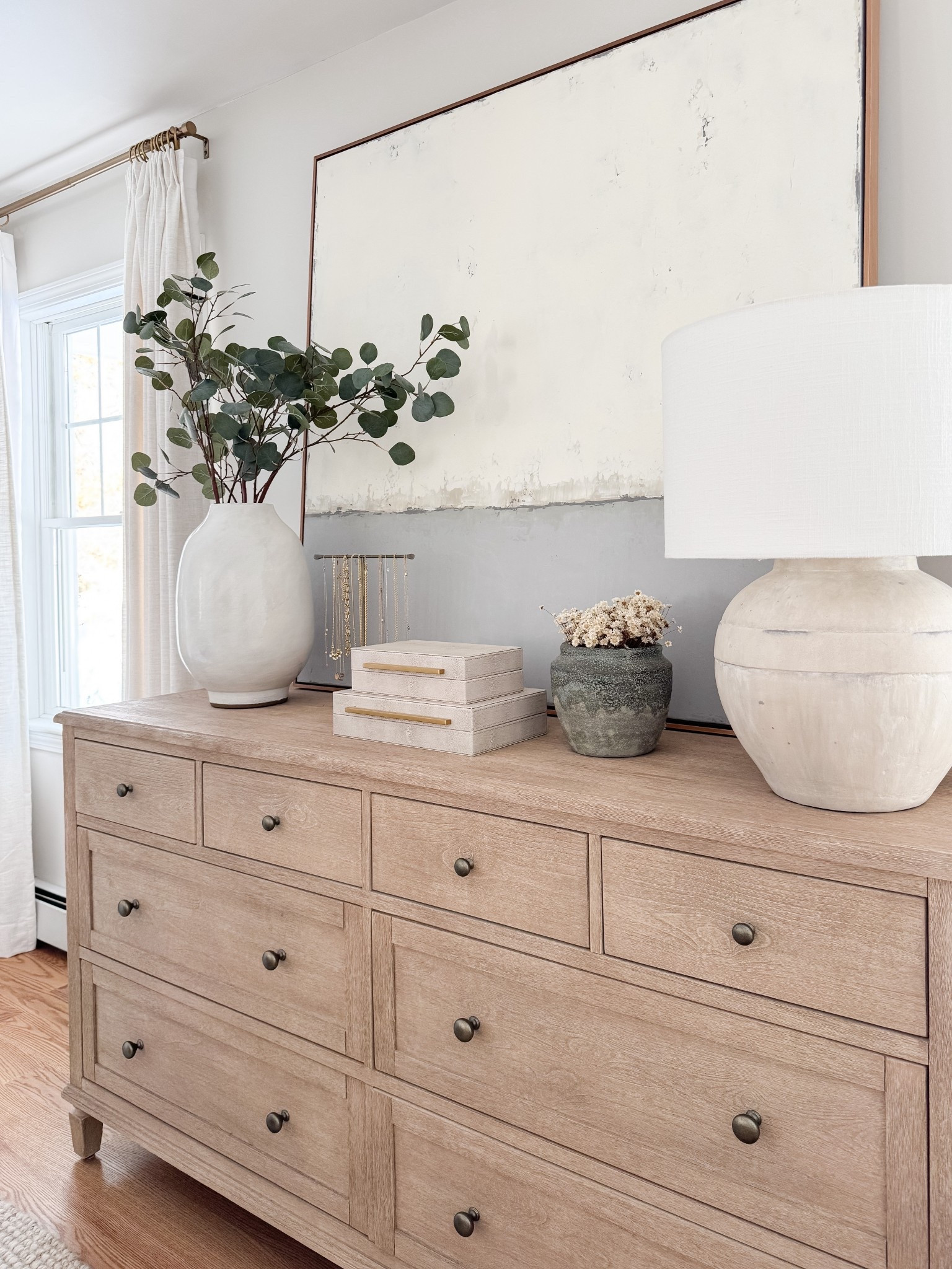 Light wood dresser styled with oversized neutral artwork, ceramic table lamp, stacked decorative boxes, and greenery in a white vase. Balanced, minimal coastal styling for a serene bedroom. 
dresser decor, bedroom dresser styling, oversized wall art, neutral artwork, decorative boxes, ceramic lamp, greenery vase, coastal bedroom decor, light wood furniture, minimalist home decor, organic modern bedroom, styled surfaces, sherri calnan home

#LTKHome